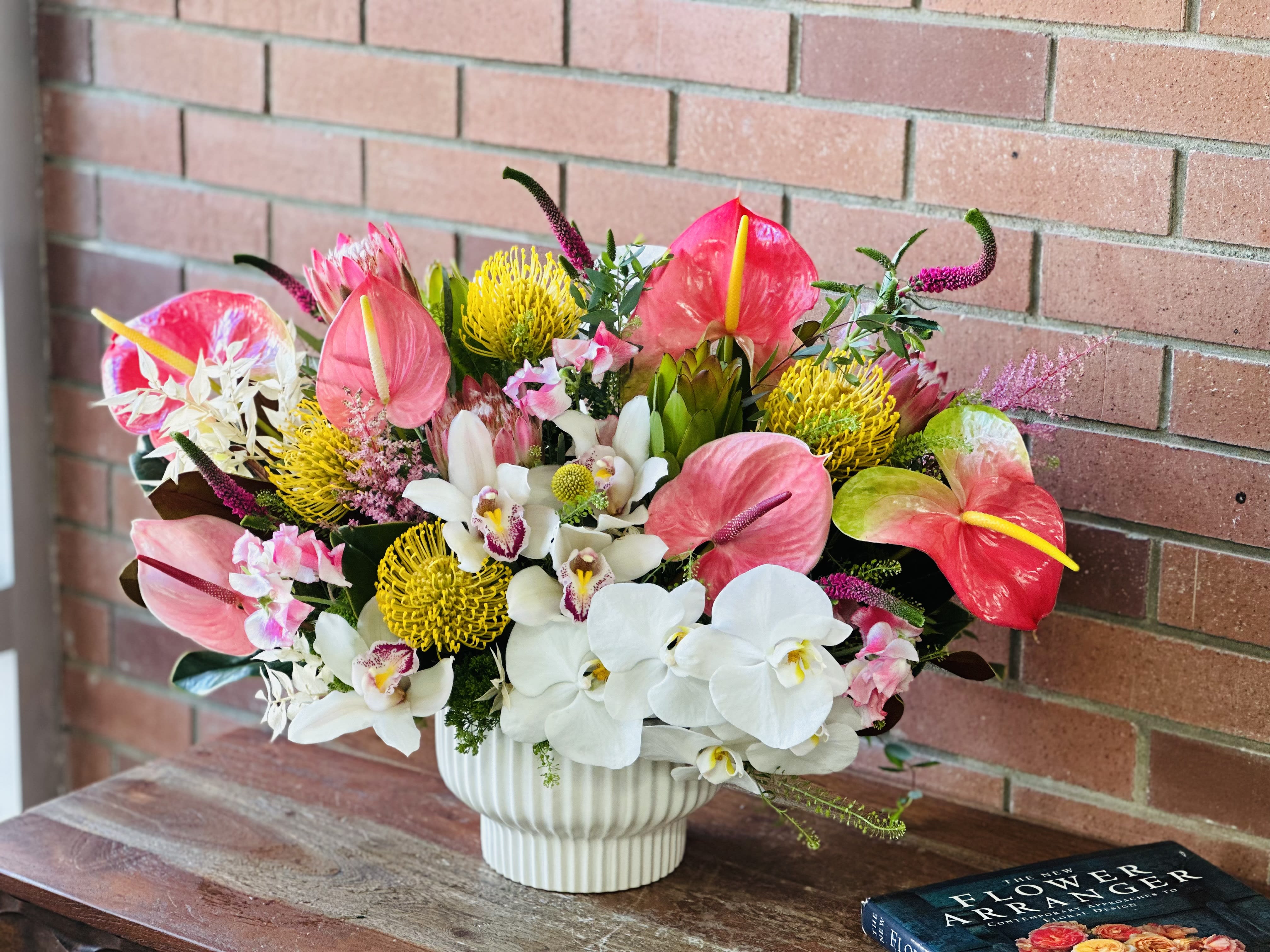 Venetian Signature Tropical Arrangement  - Modern ceramic vase - The Venetian Signature Tropical Arrangement is a stunning display of white Phalaenopsis orchids, cymbidium orchids, anthurium, yellow exotic pin cushion proteas, safari sunset, Veronica, sweet peas and lush filler flowers and tropical foliage. This bouquet is a 360 design