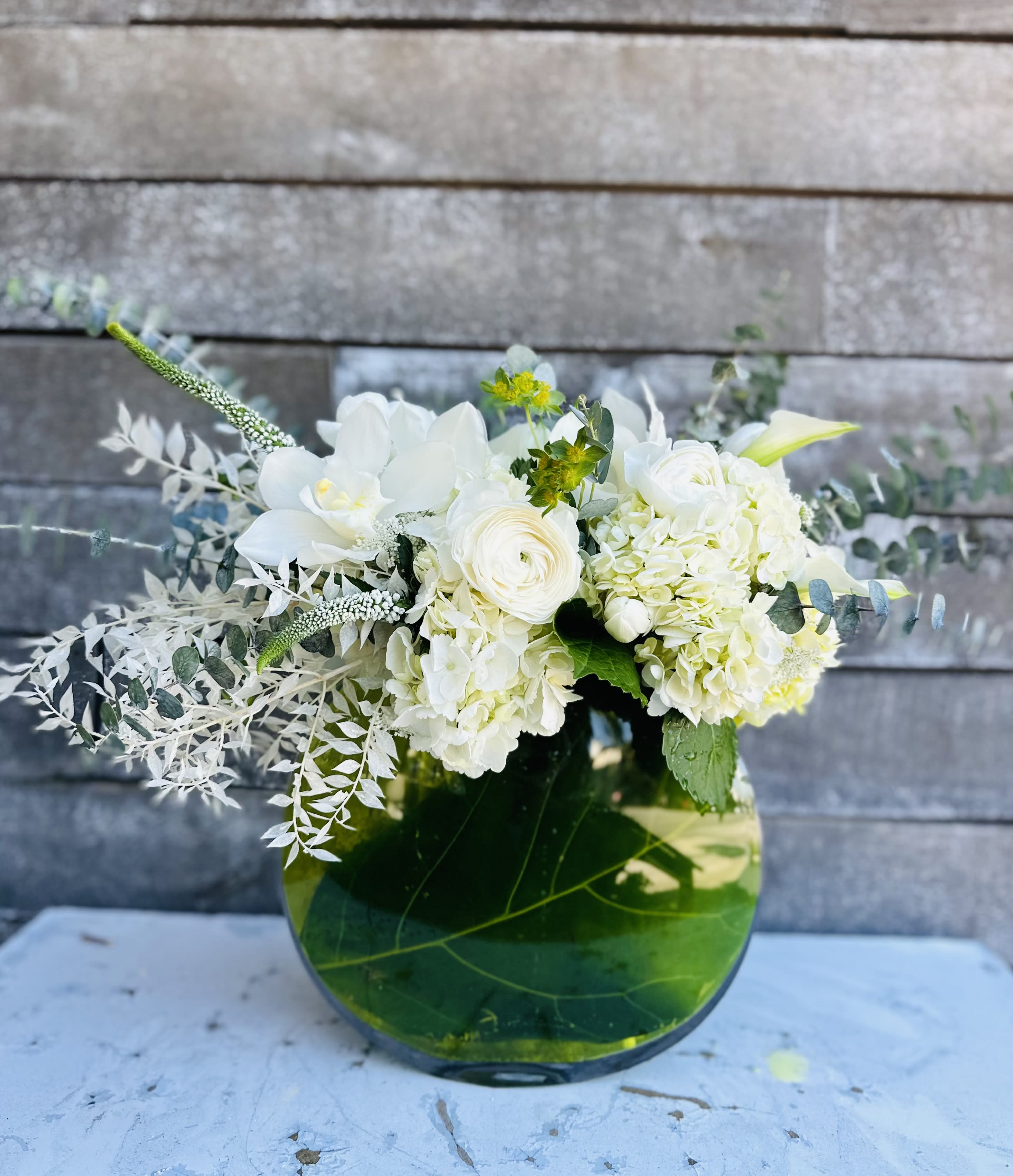 Fiddle luxe  - Fiddle fig leaves inside of an oval glass container with a spray of gorgeous white flowers including orchids on the top