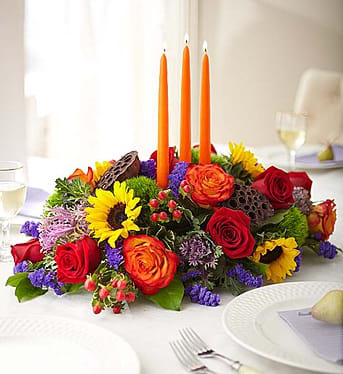 Garden of Grandeur Autumn Centerpiece - We’ve re-imagined one of our most impressive fall bouquets as a luxurious centerpiece! Radiant roses and sunflowers are hand-gathered with a mix of brightly colored blooms and unique accents, creating a truly eye-catching arrangement. A trio of orange candles adds the perfect finishing touch for a season full of spirited celebrations with the people you hold closest to your heart.