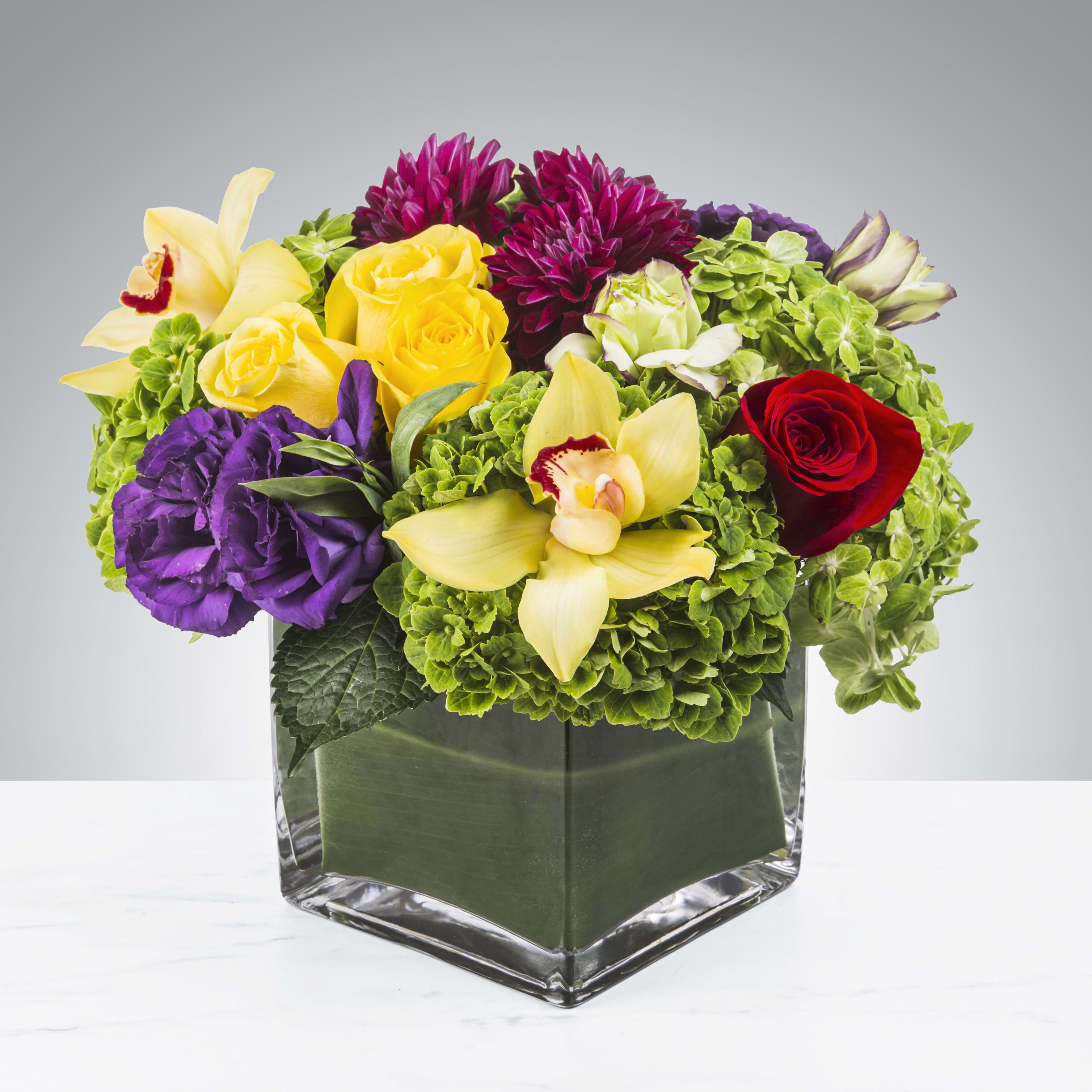 Along for the Ride by BloomNation™ - This multicolored arrangement includes roses, dahlias, orchids, lisianthus and hydrangeas in a large cubed vase. Along for the Ride by BloomNation™ is the perfect way to send a little kindness.   APPROXIMATE DIMENSIONS 12&quot; W X 12&quot; H