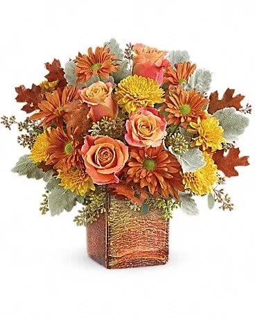 Teleflora's Grateful Golden Bouquet - Two fabulous fall gifts in one, this lovely autumnal bouquet is hand-arranged in an opalescent mercury glass cube with golden ombre finish. Beautiful bi-colored orange roses are arranged with yellow cushion spray chrysanthemums, orange daisy spray chrysanthemums, seeded eucalyptus, dusty miller, and brown transparent oak leaves. Delivered in a Golden Amber cube.