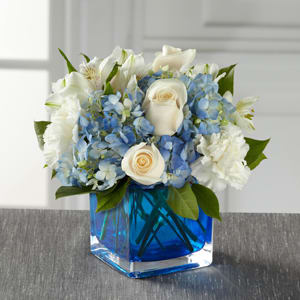 Hanukkah Bouquet - A soft, charming, and stylish flower bouquet, this arrangement exudes warmth and light in celebration of Hanukkah helping you celebrate with those recipient's close to your heart. Clouds of blue hydrangea standout amongst the clean white of roses, carnations, and Peruvian Lilies accented with lush greens while seated in a modern blue glass 