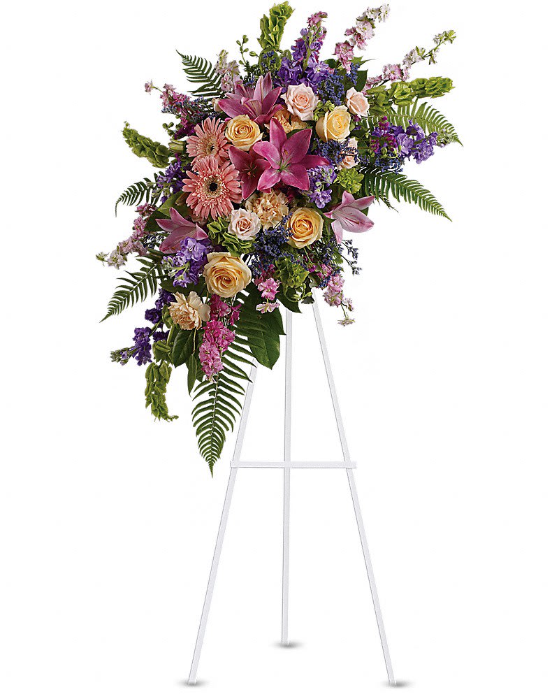 Touching Moments Spray - A sublime garden of rich yet subtle hues is a touching tribute to a lifetime of memories and special moments as varied and dear as this palette of blooms. A lovely assortment of flowers such as pink roses larkspur asiatic lilies gerberas and sinuata statice with peach roses and carnations purple stock and limonium and bells of Ireland on a classic easel.