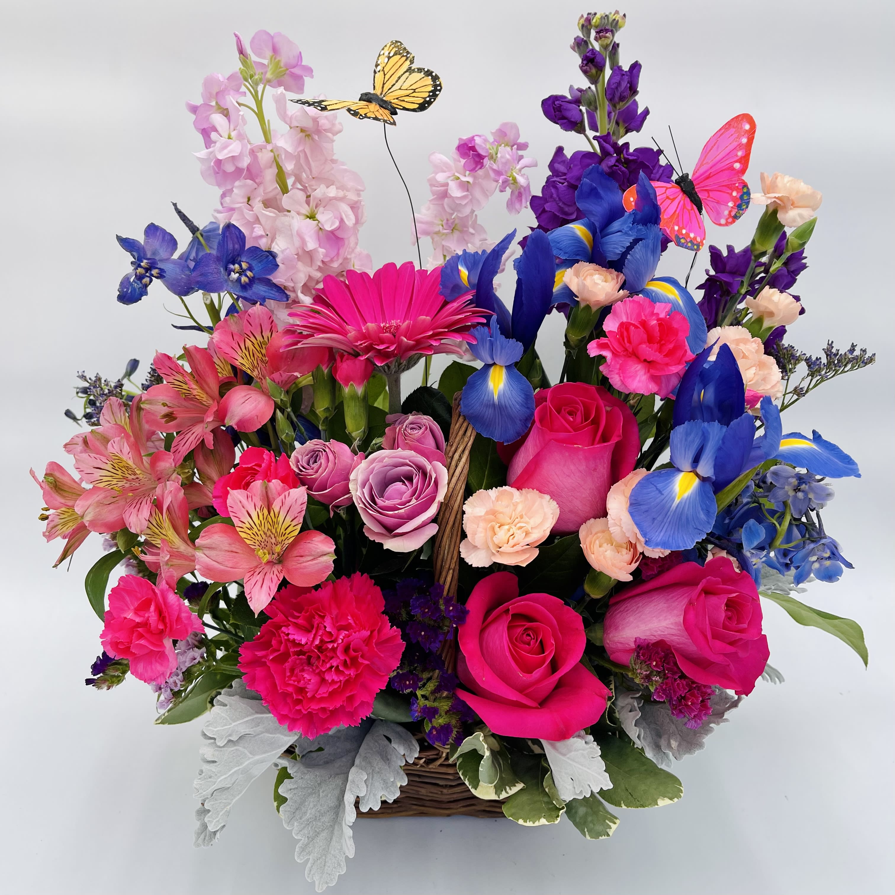 Country Meadow Basket - Enjoy the beauty of the countryside blooms with our County Meadow Basket.  Celebrate springtime with friends and loved ones with this arrangement of pink and purple blooms with playful butterflies floating above.  Basket includes roses, carnations, alstromeria, iris, stock, and assorted greenery.  Our florists handcraft these arrangements to be as fresh as possible, so certain flower varieties and colors may vary.