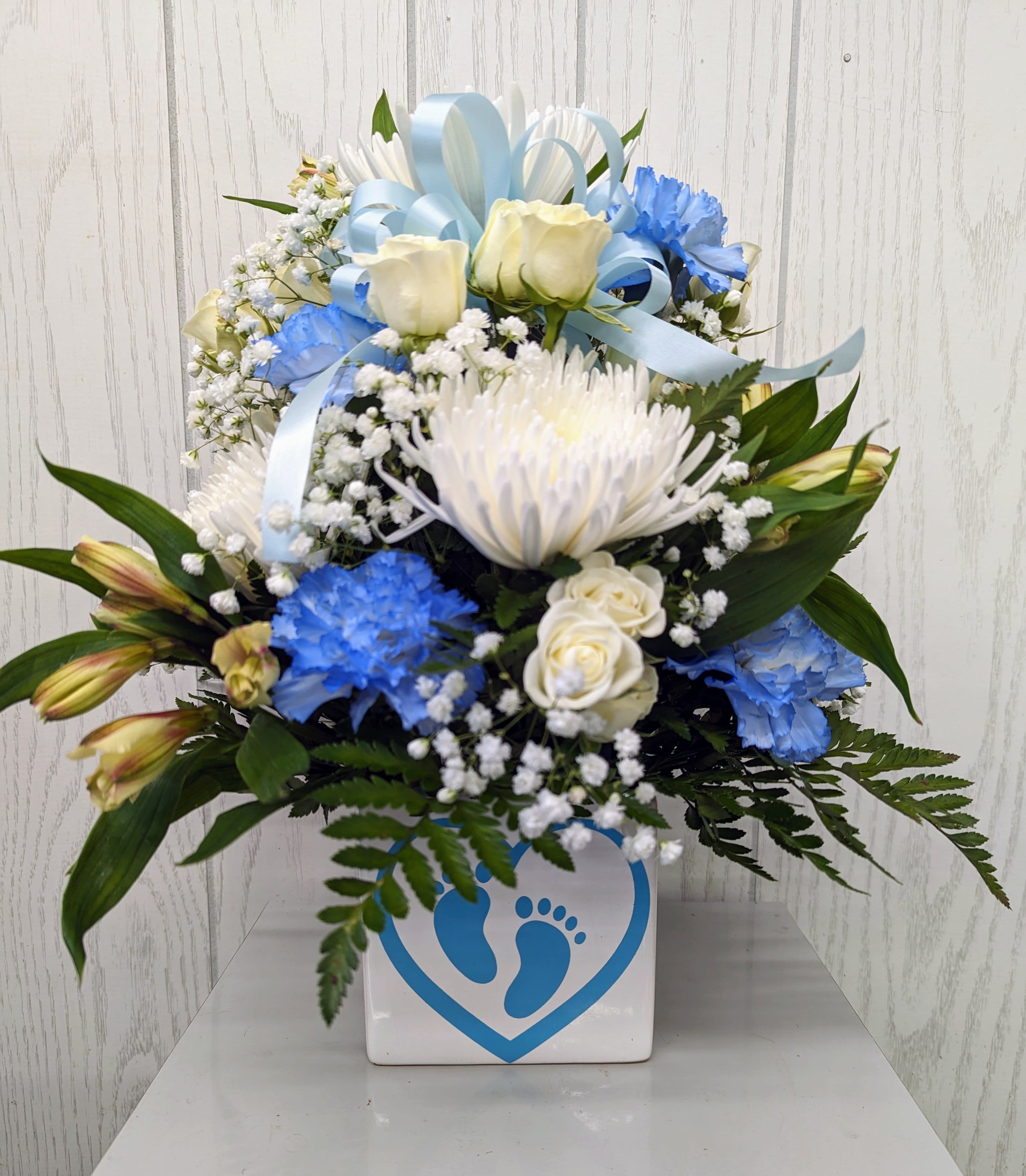 Pitter Patter Baby Boy Bouquet Pitter Patter Baby Boy Bouquet - Celebrate the baby boy with this adorable ceramic container featuring a custom decal. One-sided and approximately 17 inches tall. Featured flowers may vary due to product availability. Deluxe and Premium include additional flowers.