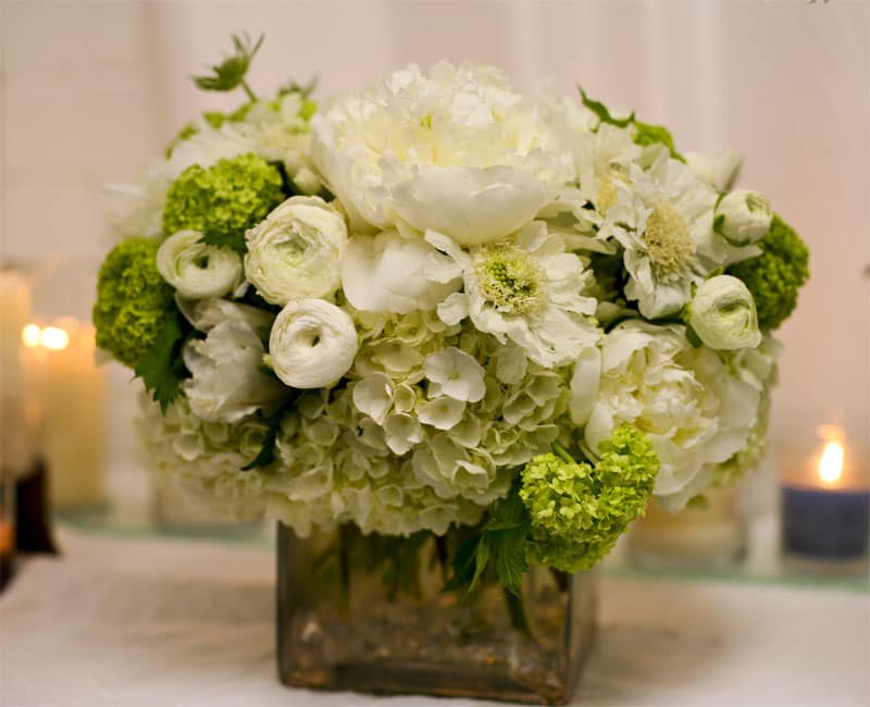 Vintage - A delicate collection of flowers--green and white hydrangea, viburnum, white ranunculus, and white peonies--create a beautiful arrangement that adds a soft vintage touch in a square glass vase lined with crystal beads.  vase: 6x6 in