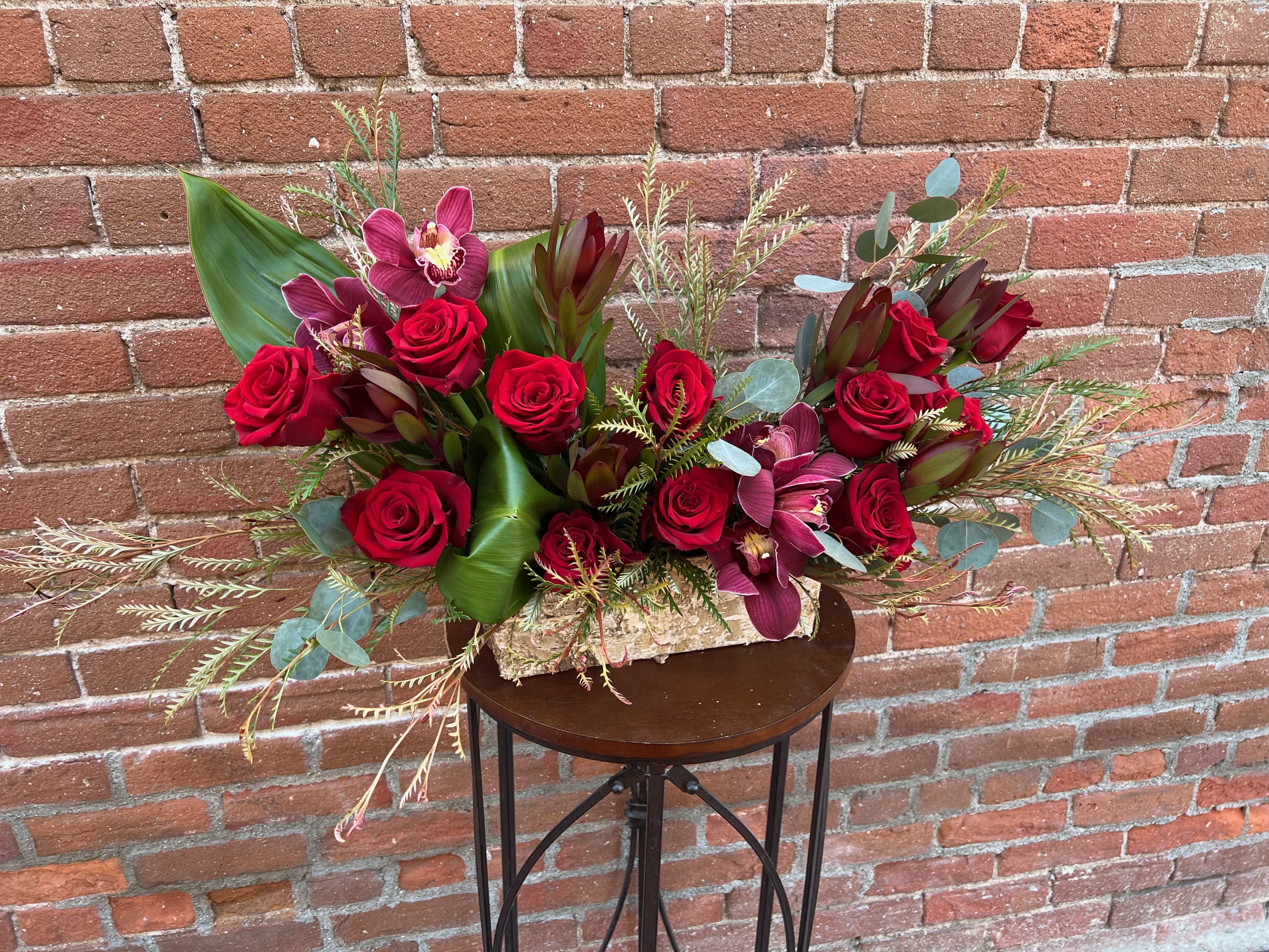 falling in Love falling in Love - a decadent dozen rose arrangement filled with our selection of fall leaves, burgundy orchids and stunning safari sunset proteas