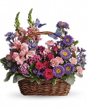 Country Basket Blooms - Talk about a bountiful basket! This wicker basket is overflowing with beauty and blossoms. It's no wonder two pretty butterflies have made this basket their home. Hot pink spray roses, light pink alstroemeria, snapdragons and miniature carnations, dark pink Sweet William, purple matsumoto asters, large monte cassino asters, statice and pittosporum fill a pretty picnic-like basket. You've got this gift handled!