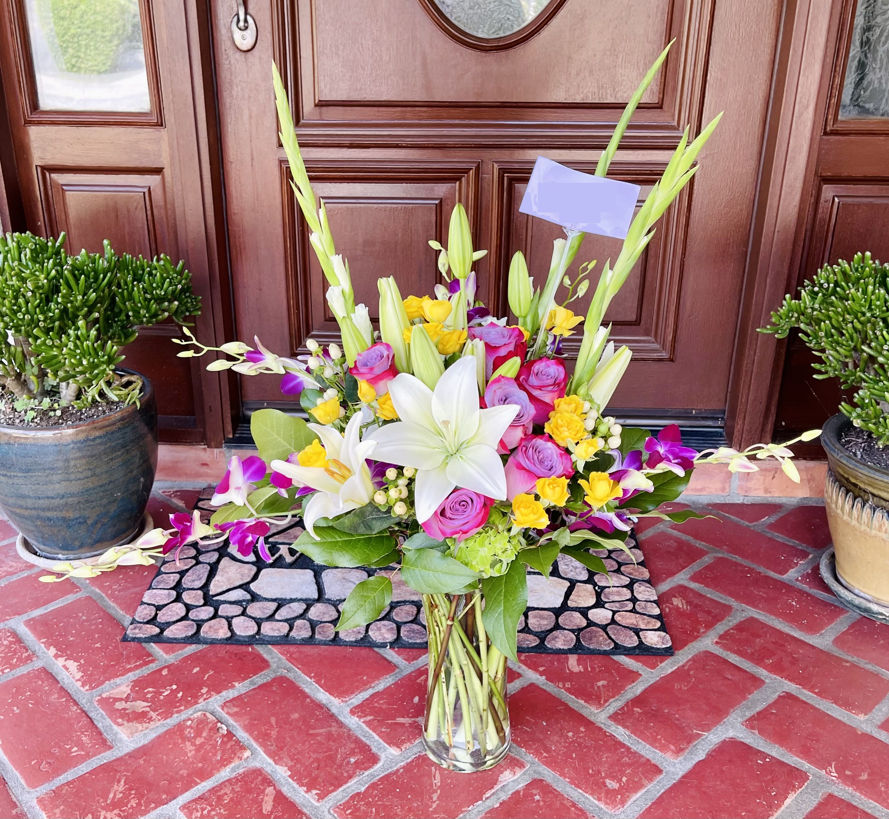 Rays of Splendor - A beautiful bouquet of lavender roses, purple orchids, yellow spray roses, green hydrangea white tiger lilies, gladioli and coffee bean in a clear glass trumpet vase.  Our florists hand-design each arrangement, so colors and varieties may vary due to availability.