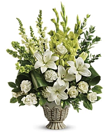 Teleflora's Clouds Of Heaven Bouquet - As serene as gently falling snow, this elegant white arrangement in a large antiqued pot is a heartfelt symbol of peace and beauty, a memory that will remain a guiding light to your loved ones for years to come. White roses, white asiatic lilies, green gladioli, white carnations, bells of ireland, white snapdragons, and white stock are accented with myrtle, green ti leaves, and lemon leaf. Delivered in Teleflora's Thoughtful Tribute pot. Orientation: One-Sided