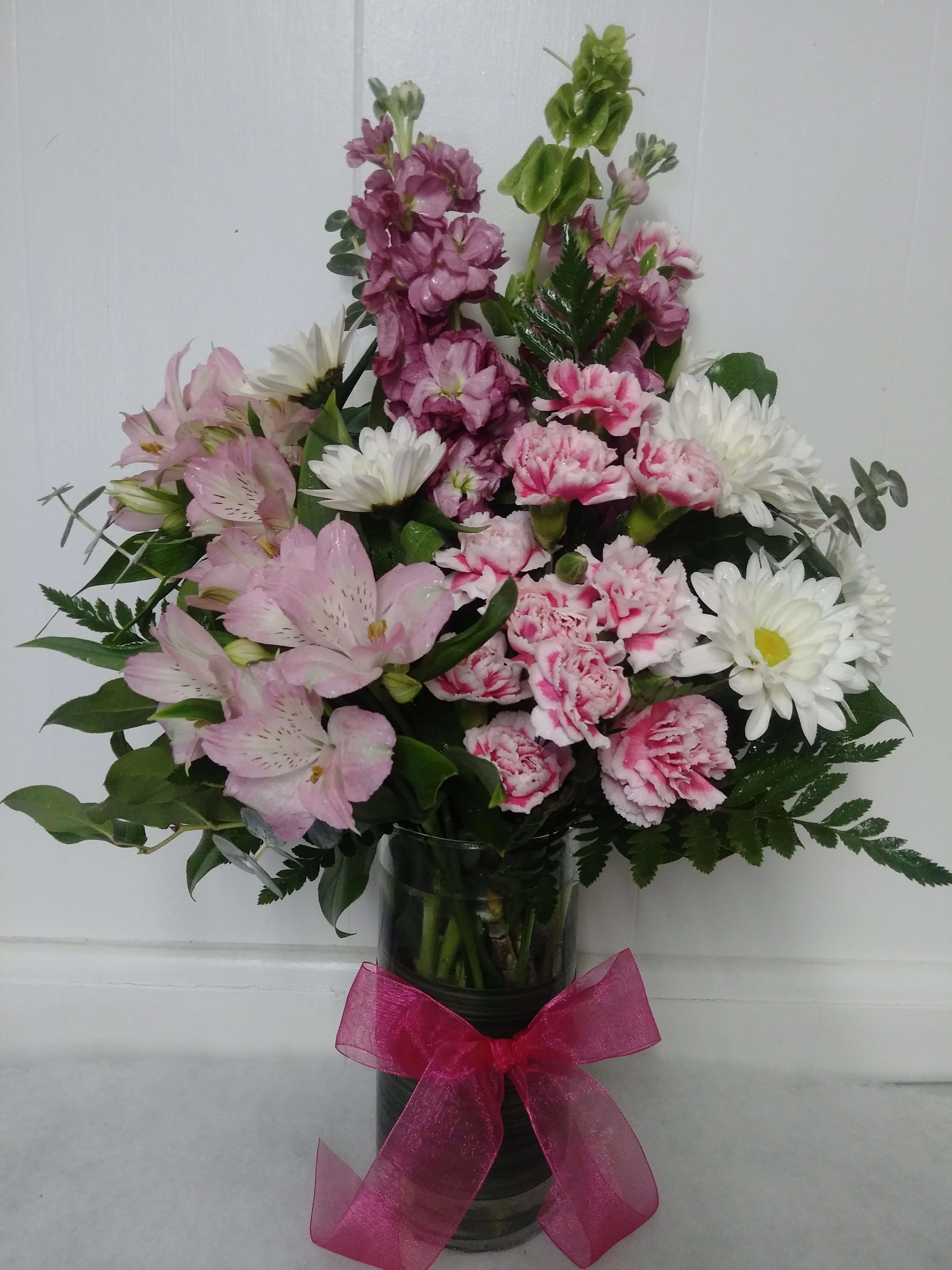 Luscious Shades Luscious Shades - Stock, alstroemeria, mini carnations and daisies with fresh greens in a clear vase wrapped wit a ti leaf ribbon and tied with a bow.