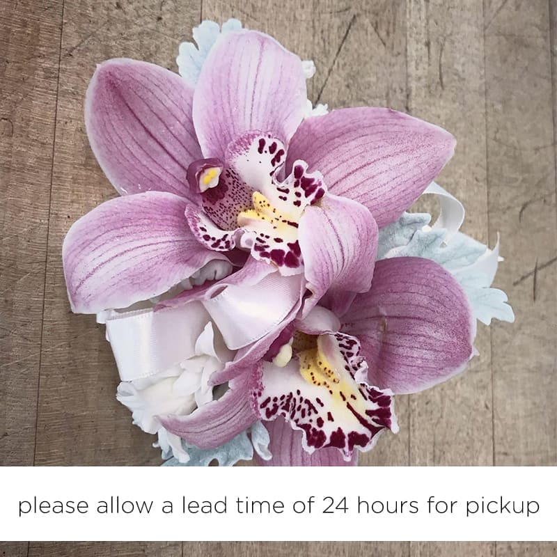 Pink Cymbidium Orchid Wrist Corsage - A wrist corsage arranged with pink cymbidium orchids and white floral accents. :: Our wrist corsage are custom-made to fit your event colors. :: Please let us know the colors or give us a call for ideas. :: Allow A Lead Time Of 24 Hrs To Pick Up Please specify time for pick up and other changes on the special instructions box at check out.  please indicate Pick Up time on special instructions box. Flowers may be subject to market availability. Thank you. ::