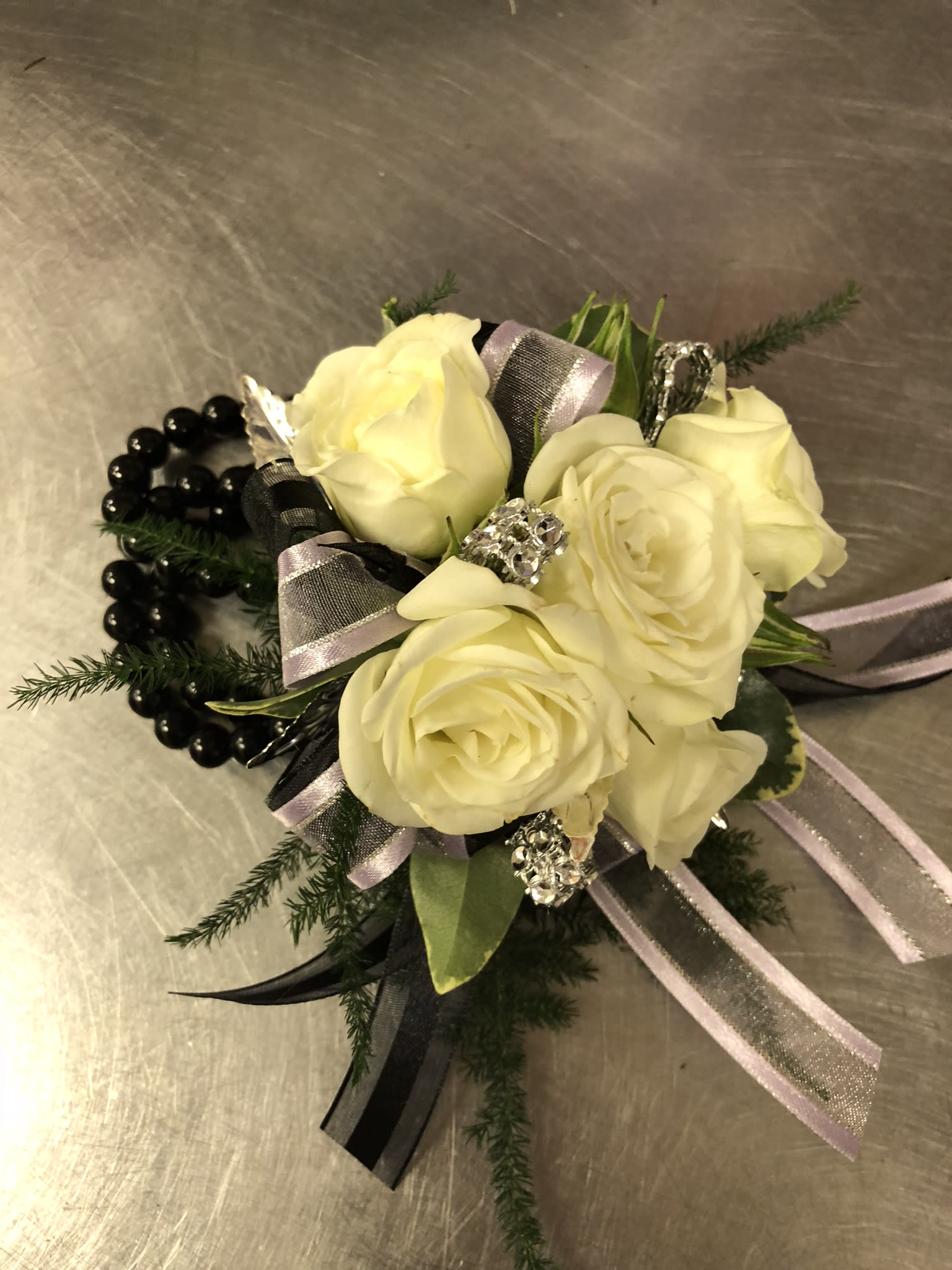 Corsage Black and White - Our corsages are made to order, in the special instruction box let us know what color you would like the flower and the ribbon to be. It also helps to know the dress color and the accent colors (like the color of the jewelry or shoes). Pictured is white ribbon and roses with silver accent rhinestones and a black pearl keepsake bracelet.