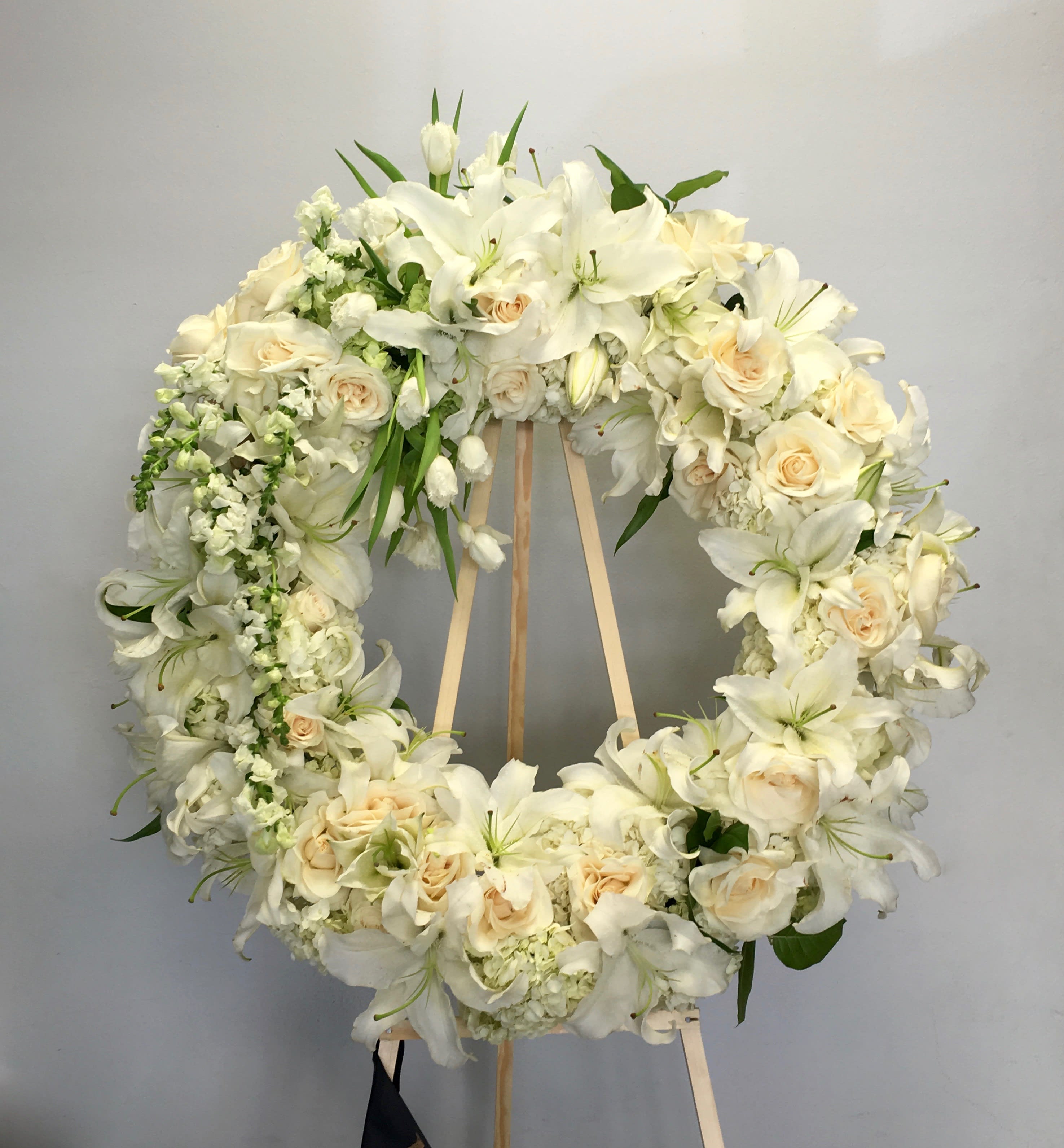 Starry Eyed Wreath  - This wreath includes bright white stargazer lilies, roses, and seasonal greens.  First photo shows standard size, second photo shows deluxe size.  We include easel, printed banner and delivery (some fees may apply).  Standard size is 30'', deluxe is 36'', and premium is 42''.