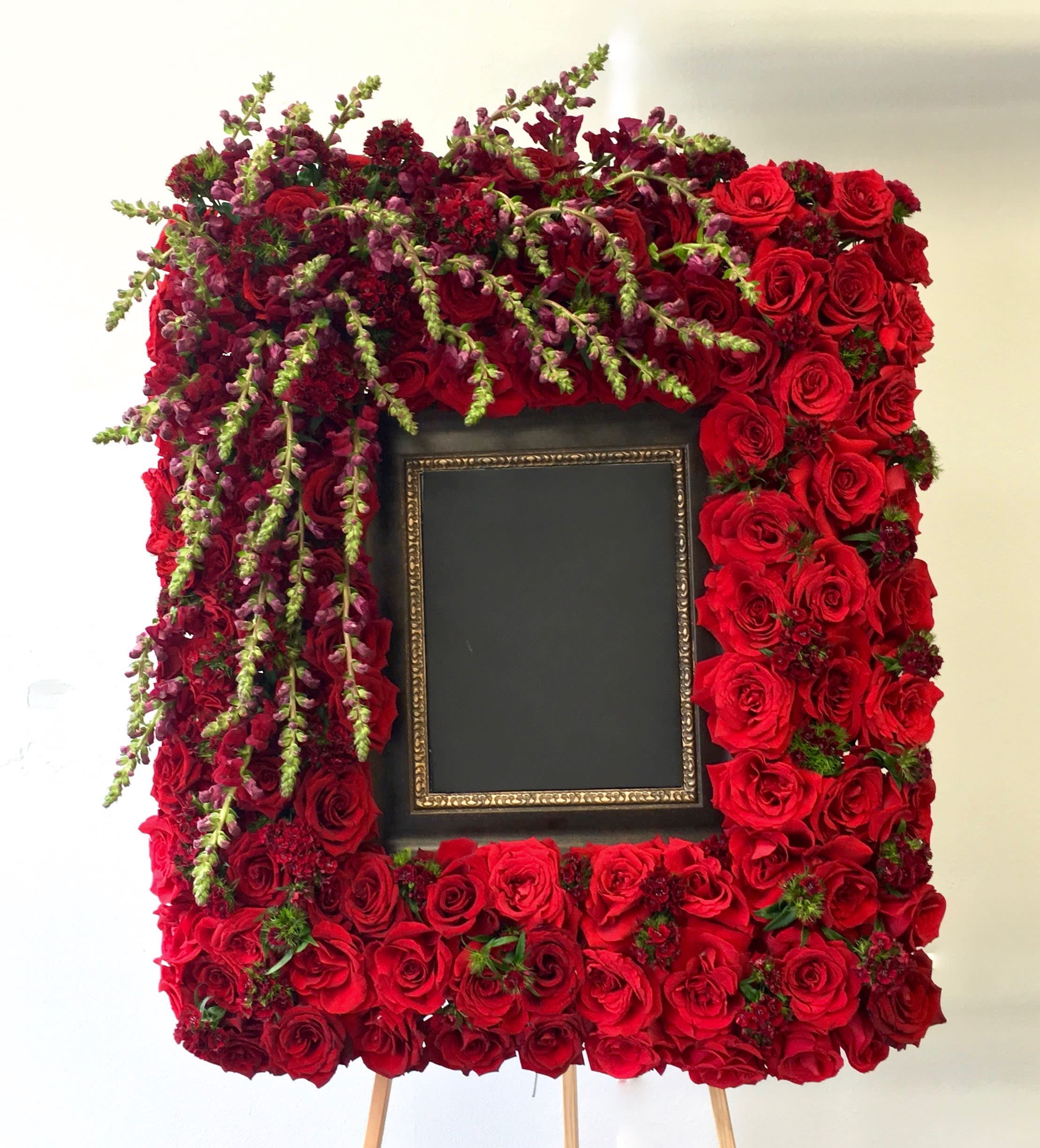 Red Rose Frame  - This frame includes red roses, snapdragons and dark seasonal greens. The standard size stands at approximately 36 inches tall and 24 inches wide. Additional flowers will be added for deluxe and premium sizes.   