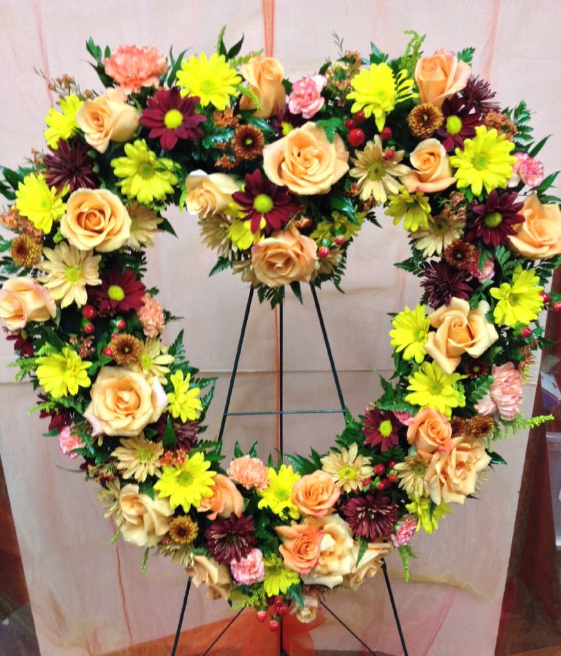 Rustic Reminiscing Heart - This beautiful rust, butterscotch, and yellow heart-shaped floral arrangement on an easel offers a calming and graceful sentiment for a funeral. The vibrant colors bring a feeling of warmth and peace, expressing an everlasting love and fond memories. The vibrant colors and floral blooms, such as roses, carnations, and daisies, bring forth a loving beauty, making it a wonderful tribute for a special memorial service.