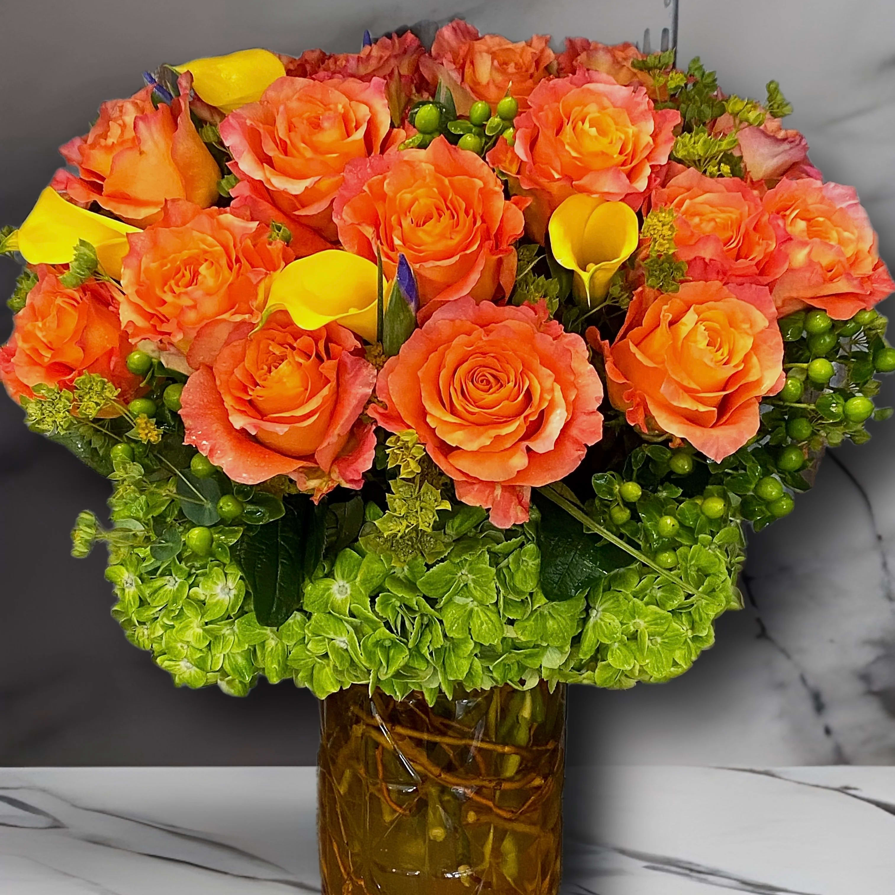 Tequila Sunrise! - Take a shot of this beautiful, bright, elevated vase arrangement filled one dozen vibrant orange roses, sunshine, yellow calla lilies, &amp; gorgeous green hydrangea, this unique vase arrangement is sure to brighten up anyone’s day! Also featuring bright, green coffee, bean &amp; branches in the water. (Vase is subject to change, depending on availability) 