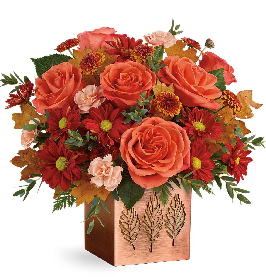 Teleflora's Copper Petals Bouquet  - Autumn shines in this festive fall bouquet! Brighten the season with this radiant rose arrangement, delivered in a shimmering copper-plated cube with punched leaf motif. They'll enjoy it for many seasons as a vase and candleholder! CONTAINER IS NO LONGER AVALIABLE. We normally use a clear orange cube instead. Unless you request something else. You can put in special instructions box.  Orange roses, peach miniature carnations, bronze daisy spray chrysanthemums, bronze button spray chrysanthemums, parvifolia eucalyptus, leatherleaf fern are accented with yellow preserved oak leaves. Delivered in a Copper Petals Cube. Approximately 13 3/4&quot; W x 12 1/2&quot; H