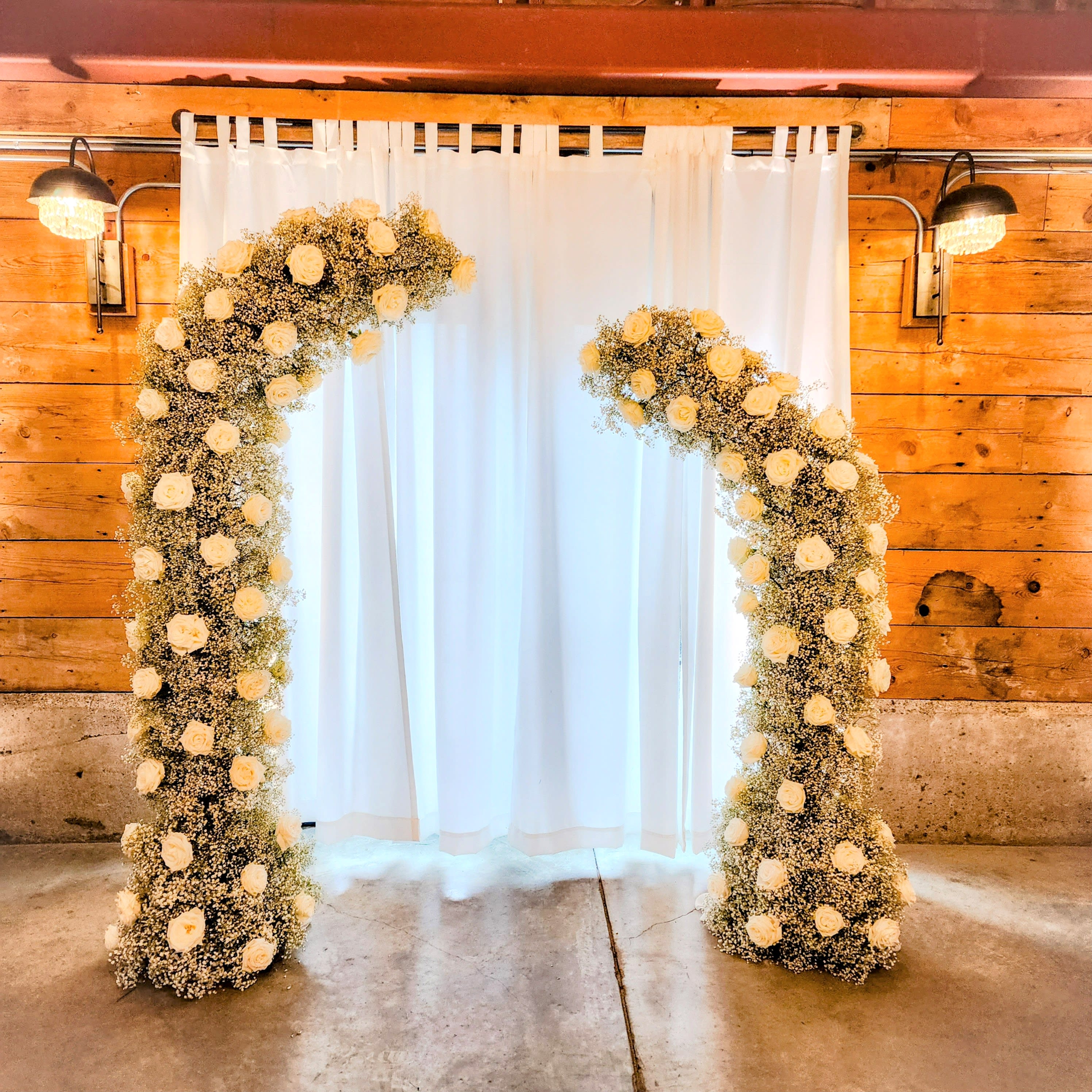 Two disjointed asymmetrical arches - Two elegant arches to frame you as you share your &quot;I dos&quot;. But, wait, they can be moved to adorn the head table as well. The arch is covered in gypsophila (Baby' Breath) and over 100 large, white roses. Rose color is easily changed.