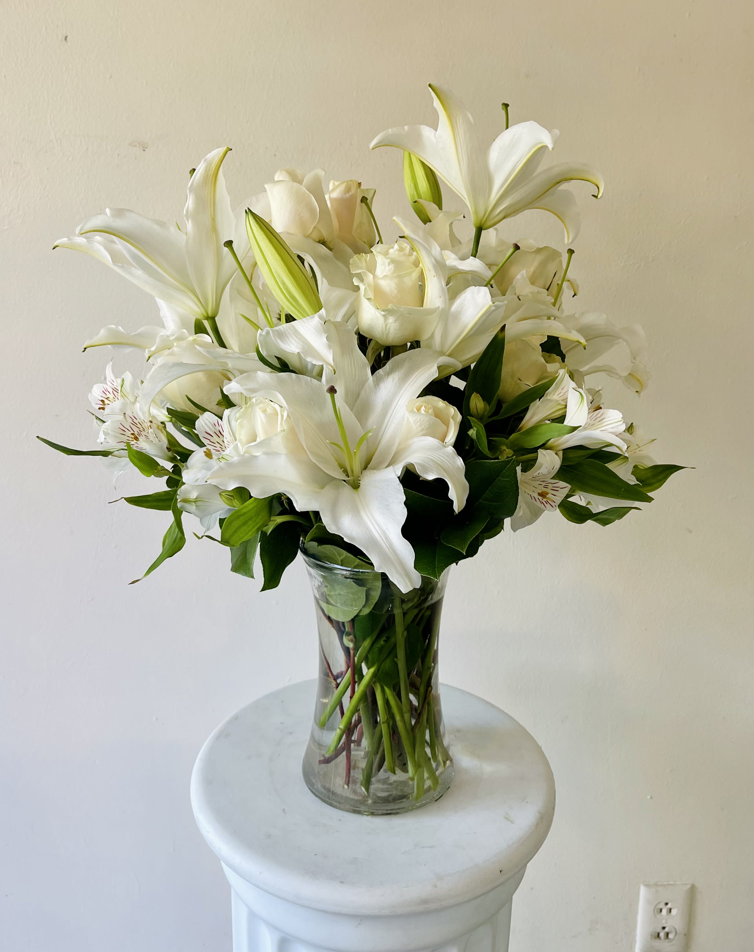 All-White Sympathy Arrangement - An elegant arrangement of white roses, lilies, alstroemeria, and greenery in a clear glass vase.  Our local florists will handcraft this arrangement to be as fresh as possible, so flower types may vary depending on availability.