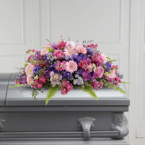 The FTD Glorious Garden Casket Spray - Colorful full and lush this extraordinary casket spray makes a memorable and touching statement of sympathy that’s sure to be a comfort to grieving family and friends. This vibrant mixed flower casket spray is a generously scaled floral creation of bright and blue spring color designed and constructed by a local FTD artisan florist and includes pink carnations cymbidium orchids and gerbera daisies hot pink roses and stock purple hydrangea and lisianthus lavender alstroemeria Monte Casino and limonium all accented with lush greens. It’s made to fit over the closed portion of a casket cover during visitation at a funeral home at a funeral service and at a graveside ceremony at the cemetery.