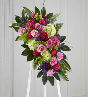 The FTD Refreshing Mix Standing Spray - This glorious celebration of life combines the vibrant hopeful colors of spring in a standing arrangement designed to inspire happy memories of times gone by. Handcrafted by a local FTD artisan florist of bright and beautiful blossoms that include pink roses magenta carnations purple statice and hydrangeas green button pompons and hydrangeas and daisy pompons all arranged against a background of lush green aralia and aspidistra leaves. It’s designed for display on an easel making an impressive memorable expression of sympathy at a wake funeral or graveside service.