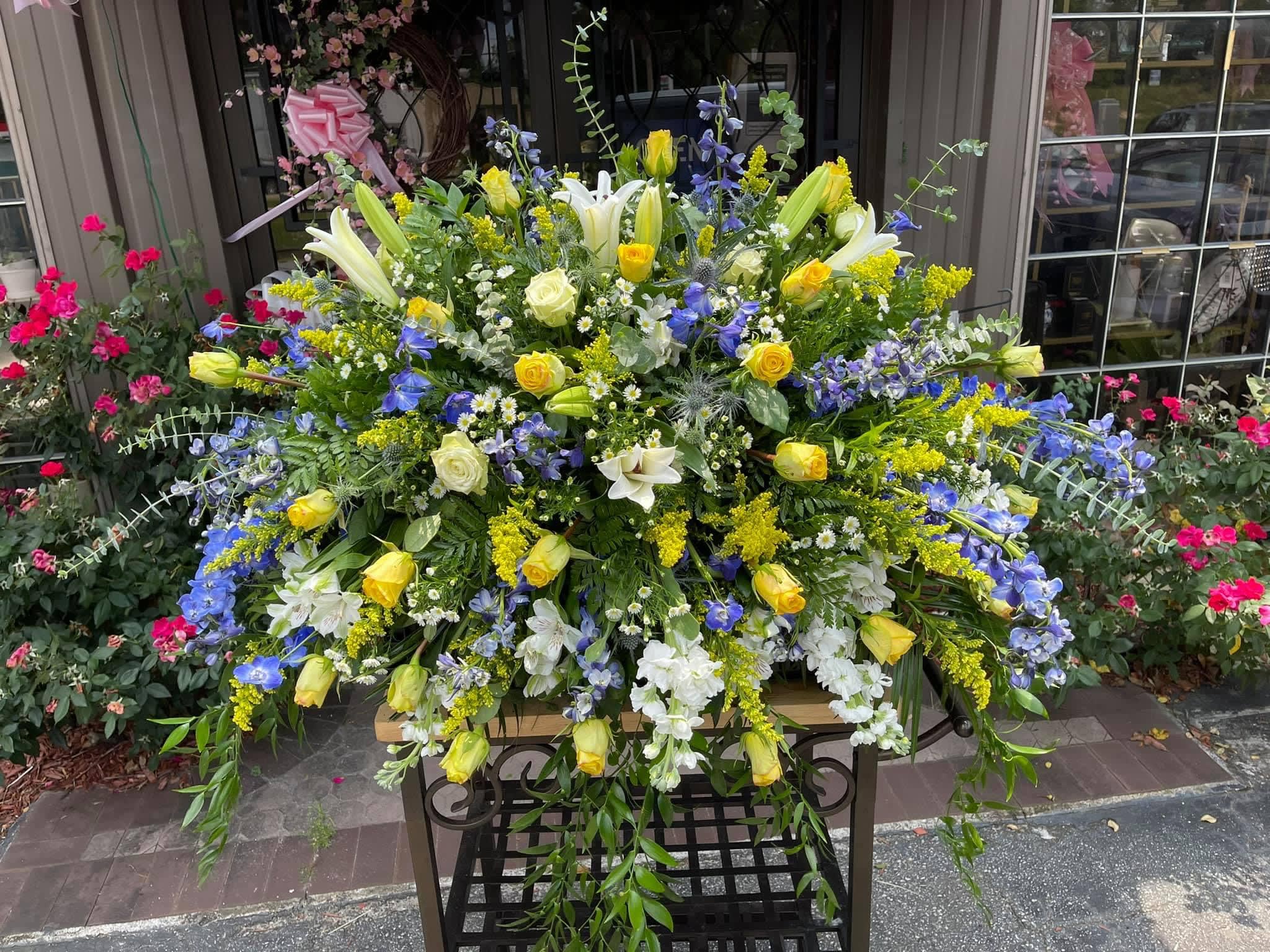 Smaller White and Blue Casket Spray Smaller White and Blue Casket Spray - Show purity of love with a mix white, yellow and blue flowers that’s as gentle and pure as a cloud. Accented with a mix of greenery, fragrant white flowers create a lovely and traditional casket spray.