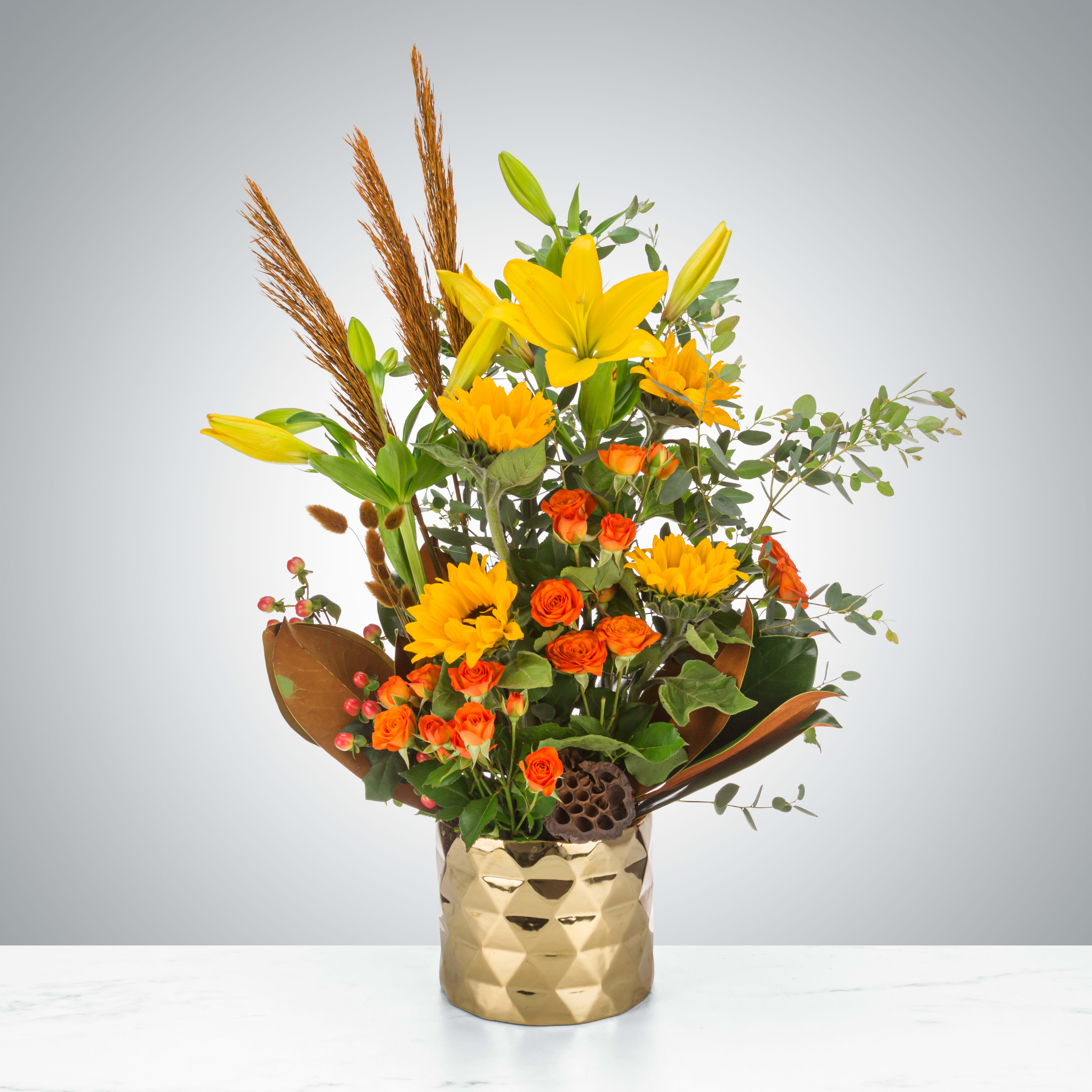 Autumn Glimmer by BloomNation™ - Autumn glimmer is a quintessential fall arrangement featuring a gold architecture vase and a variety of fun fall flowers and accents. This arrangement is pure fun and elegance with a vase that the recipient will surely re-use. Send this to impress! Perfect for the autumn equinox, Halloween or Thanksgiving.  Approximate Dimensions: 16&quot;D x 25&quot;H