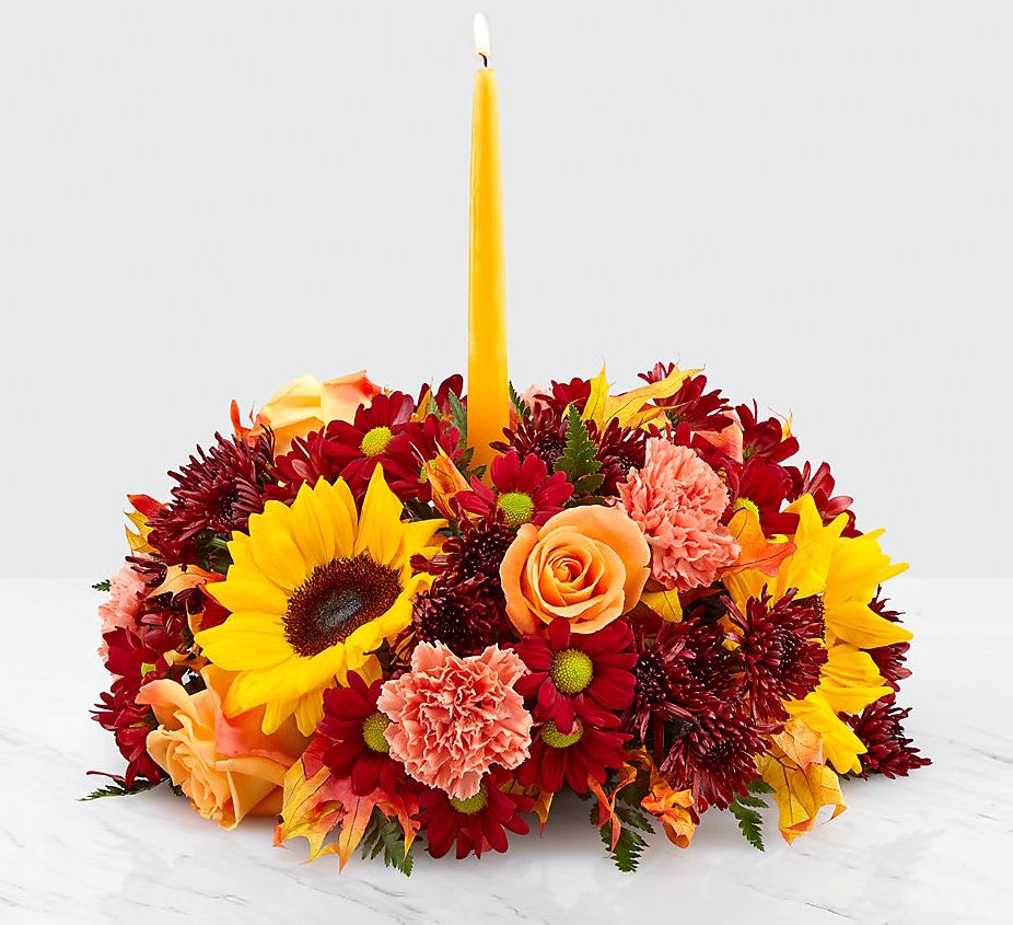 Giving Thanks Centerpiece - Gather around a gorgeous centerpiece this harvest season. Our Giving Thanks Centerpiece is sure to add a touch of heartfelt warmth to any celebration with its collection of orange roses, sunflowers, glycerized oak leaves and orange carnations set around a golden taper candle. Whether you're a guest or the host, complete the table with an elegant centerpiece sure to brighten up the room.