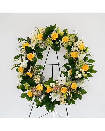 Many Blessings Wreath - This beautiful classic wreath from the Many Blessings Collection are gorgeous with fragrant white lilies, yellow roses, white orchids, stock, yellow snapdragons, antique and mini green hydrangea, with dusty miller and lemon leaf foliage.