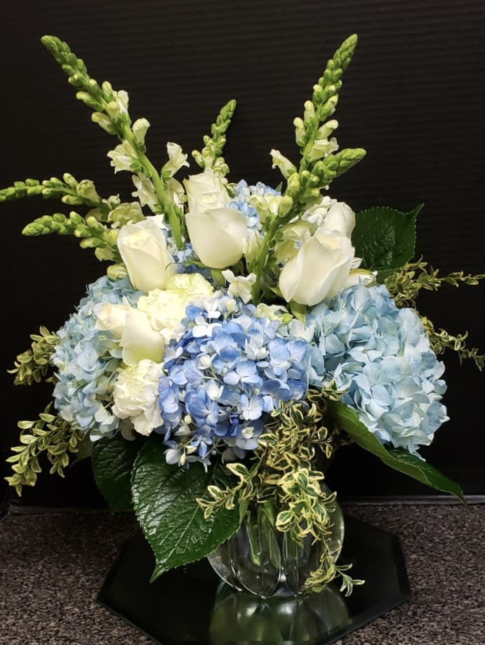  Superior Sights Bouquet - Clusters of blue and green hydrangea give this floral arrangement a fresh focus, drawing the eye with pops of  (Please always check the substitution policy before placing an order)                white roses and snapdragons perfectly placed with an artist's eye to create an unforgettable moment upon delivery. Notice how the flax leaves are placed within the arrangement to give it all a sense of movement and grace, taking the design aesthetic to a new level of sophistication. The subtle light blue color of the vase helps to bring forth the blues and greens within the bouquet, making this both a warm and airy design that will help you send a gift that truly speaks from your heart. IMPRESSIVE bouquet includes 13 stems with vase. Approx. 19&quot;H x 14&quot;W. STUNNING bouquet includes 22 stems. Approx. 21&quot;H x 16&quot;W. Large size shown 
