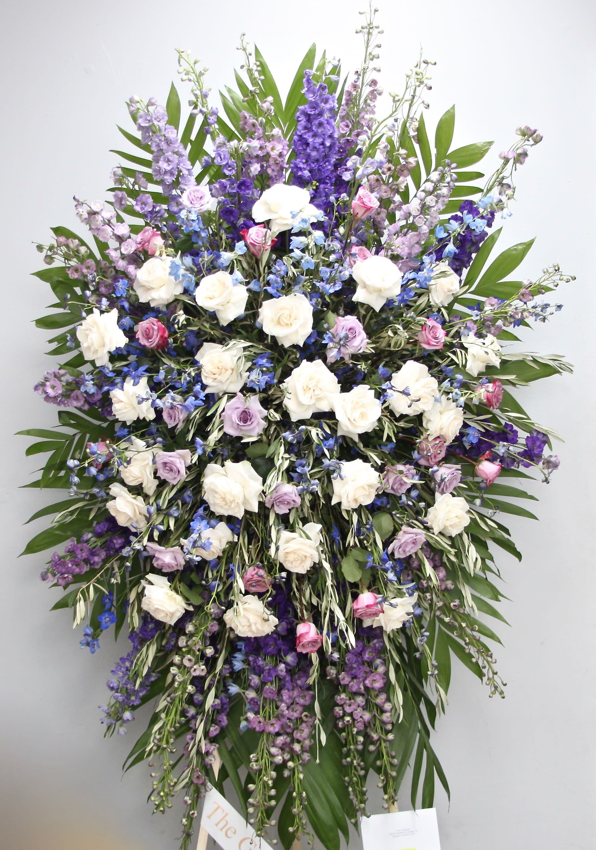 Lavender Spray  - This sympathy spray includes vibrant colors of lavender and violet. It also includes roses in white and pink and seasonal greens.   We include easel, printed banner and delivery (some fees may apply).  Standard size is 30'' wide, deluxe is 36'', and premium is 42''.