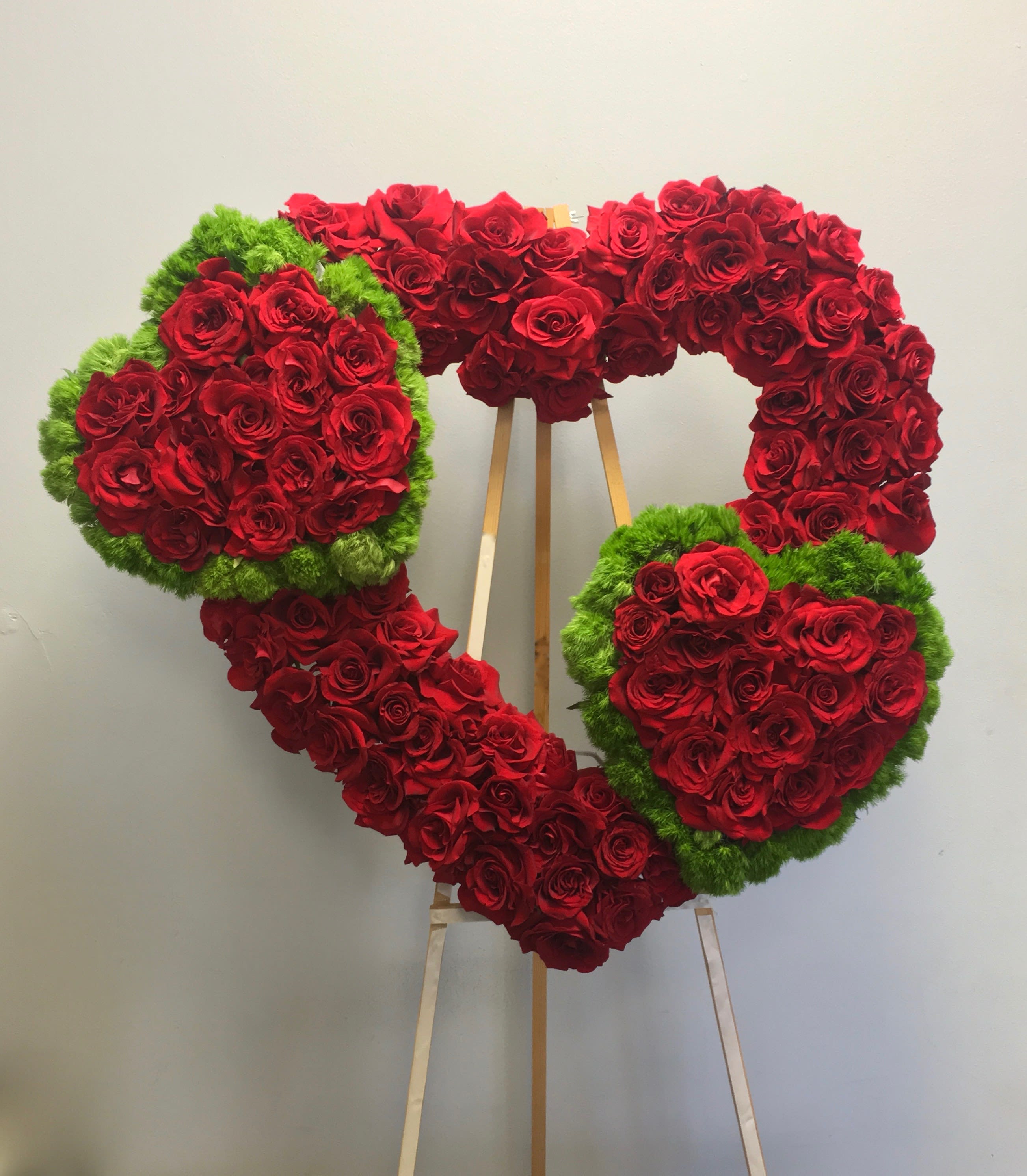 Triple Heart  - Three hearts in one, all containing red roses. The two smaller hearts are outlines in fluffy seasonal greens.   We include easel, printed banner and delivery (some fees may apply).  Standard size is 30'', deluxe is 36'', and premium is 42''. 