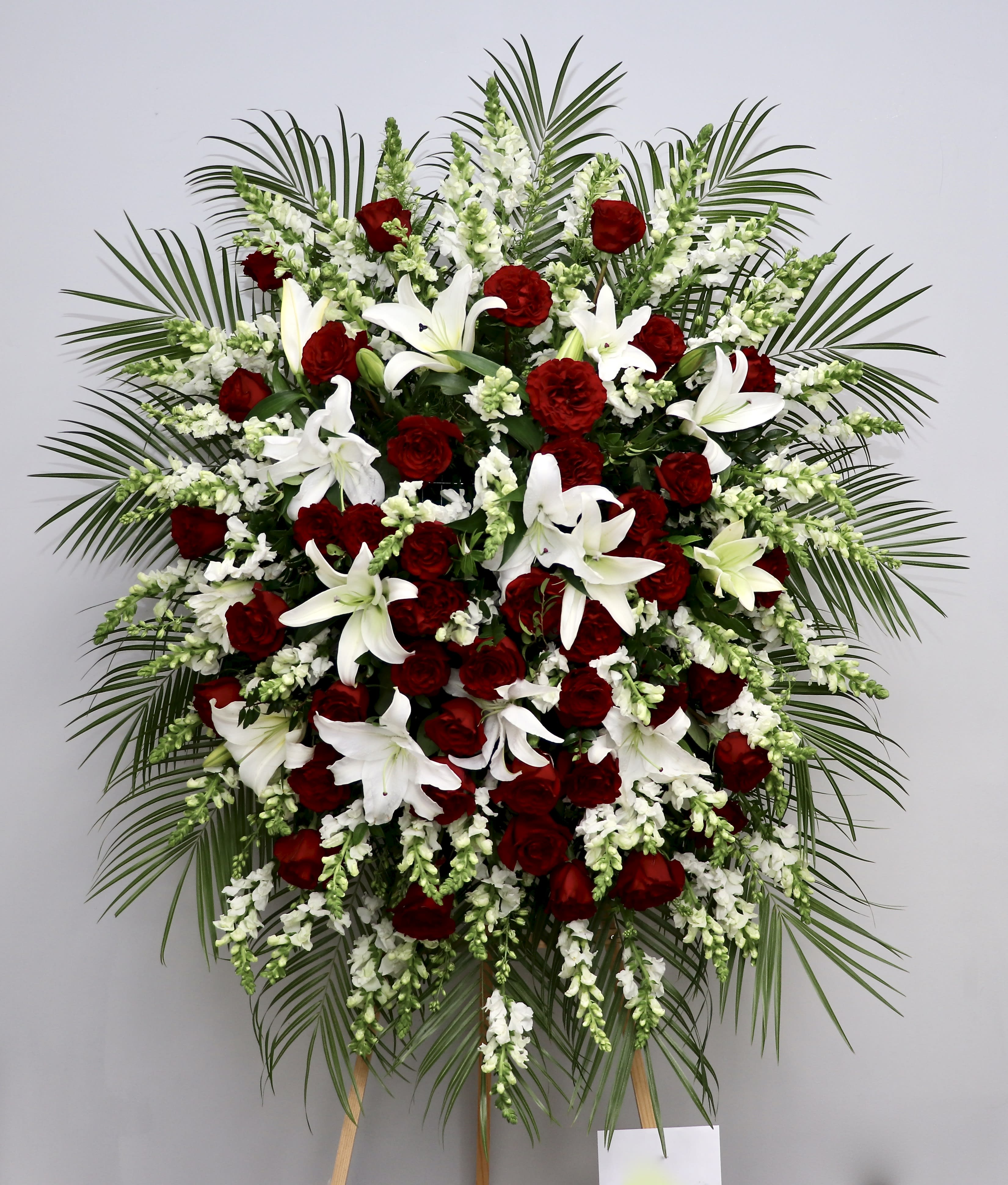 Ruby Red Spray - This spray combines red roses, lilies and snapdragons to create an elegant sympathy arrangement.   We include easel, printed banner and delivery (some fees may apply).  Standard size is 30'' wide, deluxe is 36'', and premium is 42''.