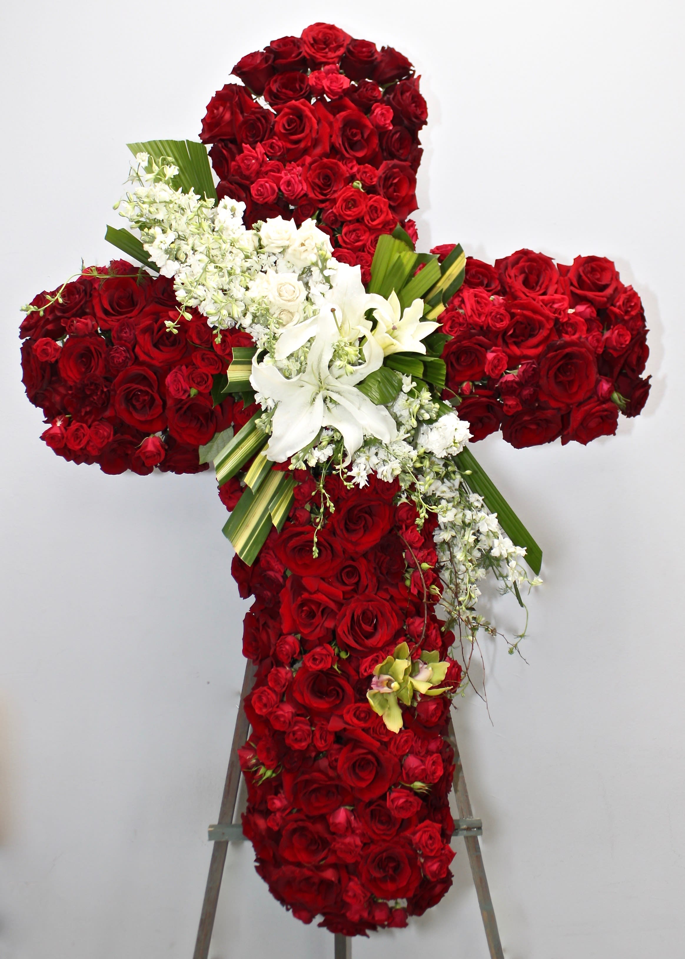 Red Rose Star Burst Cross  - This cross contains red roses of various sizes as well as a stargazer focal point. Seasonal greens and florals are also included in this cross.   We include easel, printed banner and delivery (some fees may apply).  Standard size is 30'', deluxe is 36'', and premium is 42''.