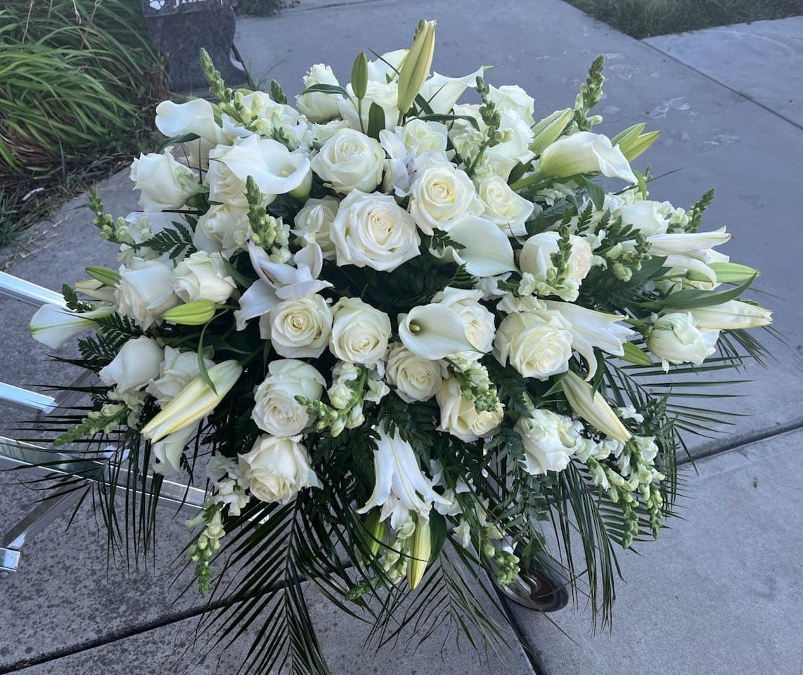 All White Casket Cover, half size - Roses, mini-callas, Casablanca lilies and other seasonal varieties make up this sophisticated casket cover. As shown is appropriate for an open-casket service. See Deluxe and Premium for closed-casket service. 