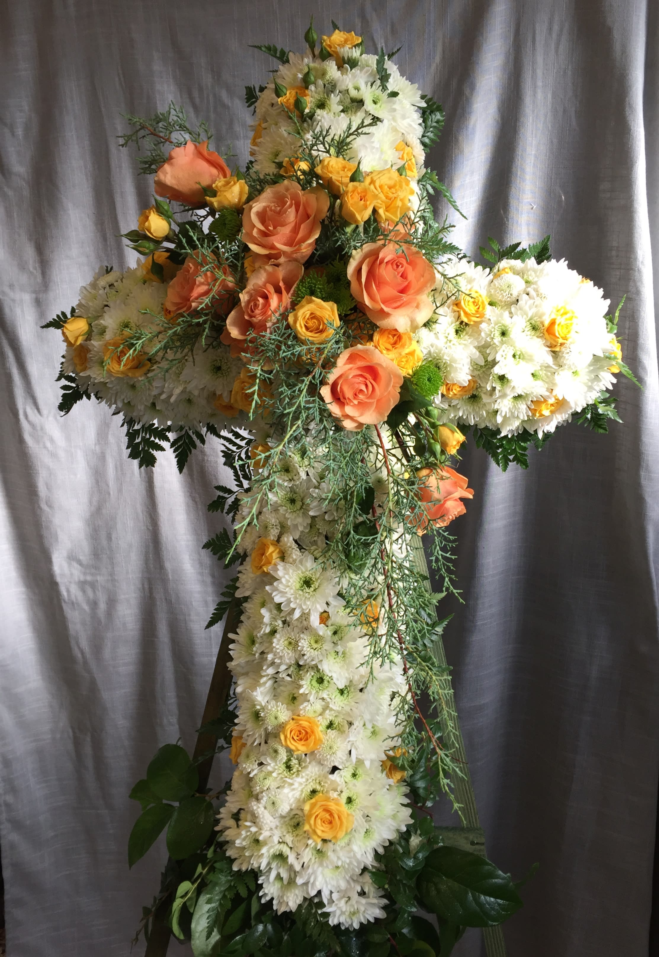 Yellow and White Cross on Stand - A white cross accented with yellow and orange seasonal blooms. Delivered on a stand.  Approximately 24&quot; across and 5 feet tall. 