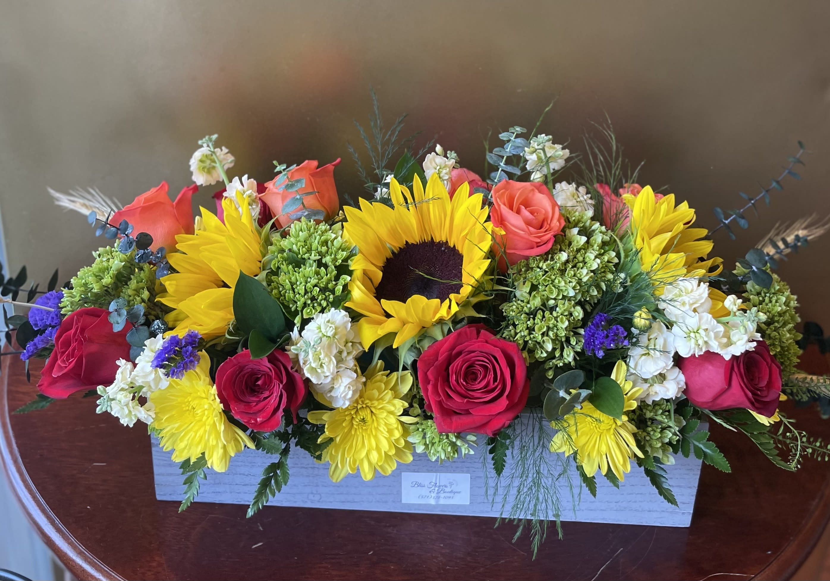 Sunny Embrace Centerpiece  - Sunny sunflowers, orange and red roses roses, yellow chrysanthemums and more - all delightfully arranged in this rustic wooden box.