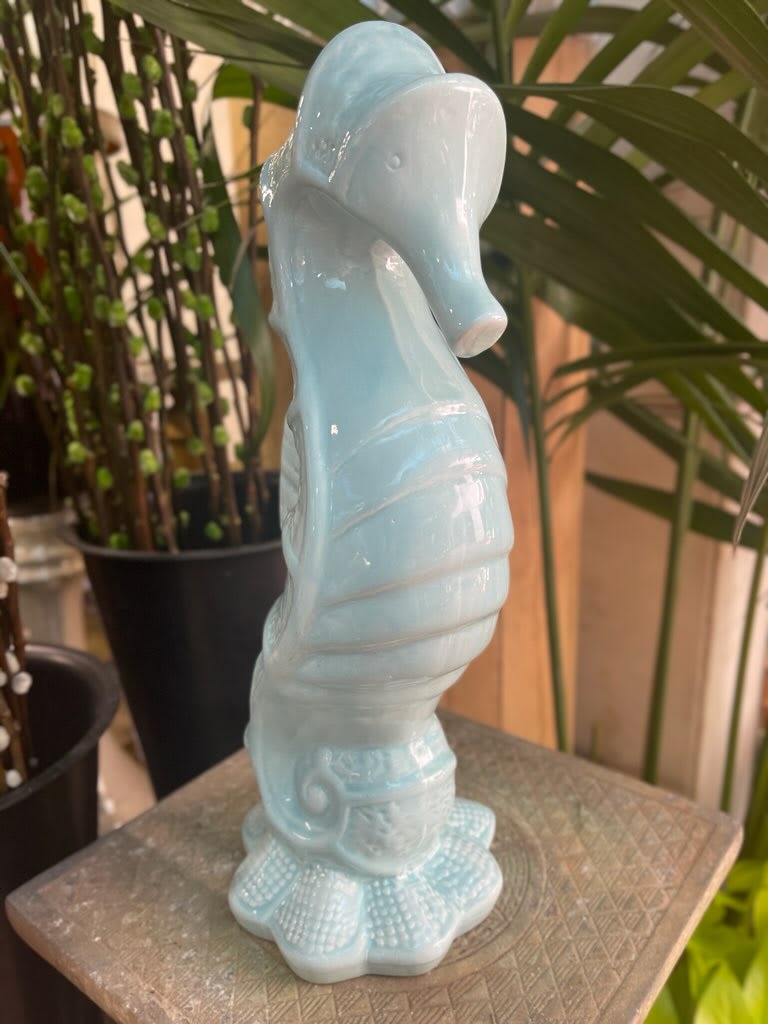 Seaside Tranquility: Ceramic Seahorse Statue with Aqua Blue Finish - Bring the calming vibes of the ocean into your home with the Ceramic Seahorse Statue featuring a soothing aqua blue finish. This elegantly crafted statue captures the essence of marine life, adding a touch of coastal charm to your living space.  Key Features:  Nautical Seahorse Design:  The statue boasts a meticulously crafted seahorse design, symbolizing the grace and beauty of the ocean's inhabitants. The nautical theme adds a coastal and relaxed ambiance to your home or office. Ceramic Construction:  Crafted from high-quality ceramic, the statue ensures durability and a smooth, polished finish. The ceramic material adds a touch of refinement to the seahorse statue, making it suitable for various decor styles. Aqua Blue Finish:  The seahorse statue features a calming aqua blue finish, reminiscent of the tranquil ocean waters. The soft blue hue adds a pop of color and complements coastal-inspired interiors. Sturdy Base:  Designed with a sturdy base, the statue stands securely on flat surfaces such as shelves, tables, or mantels. The base provides stability, allowing you to display the seahorse statue with confidence. Versatile Decor Piece:  This ceramic seahorse statue is a versatile decor piece that can be placed in various settings, from beach-themed rooms to contemporary interiors. It serves as an eye-catching accent that enhances the overall aesthetic of your space. Symbolism of Seahorses:  Seahorses are often associated with qualities such as grace, patience, and tranquility. The presence of a seahorse statue can bring these positive attributes into your living space, creating a serene atmosphere. Easy to Clean:  The smooth ceramic surface is easy to clean and maintain. Simply wipe the statue with a soft cloth to keep it looking pristine. Perfect Gift:  The Ceramic Seahorse Statue with Aqua Blue Finish makes for a thoughtful and charming gift, especially for those who love coastal decor or have an affinity for the sea. Gift it for housewarmings, birthdays, or as a unique present for ocean enthusiasts. Immerse yourself in seaside tranquility with the Ceramic Seahorse Statue in Aqua Blue Finish. This captivating decor piece brings the serenity of the ocean into your surroundings, creating a soothing and stylish atmosphere.