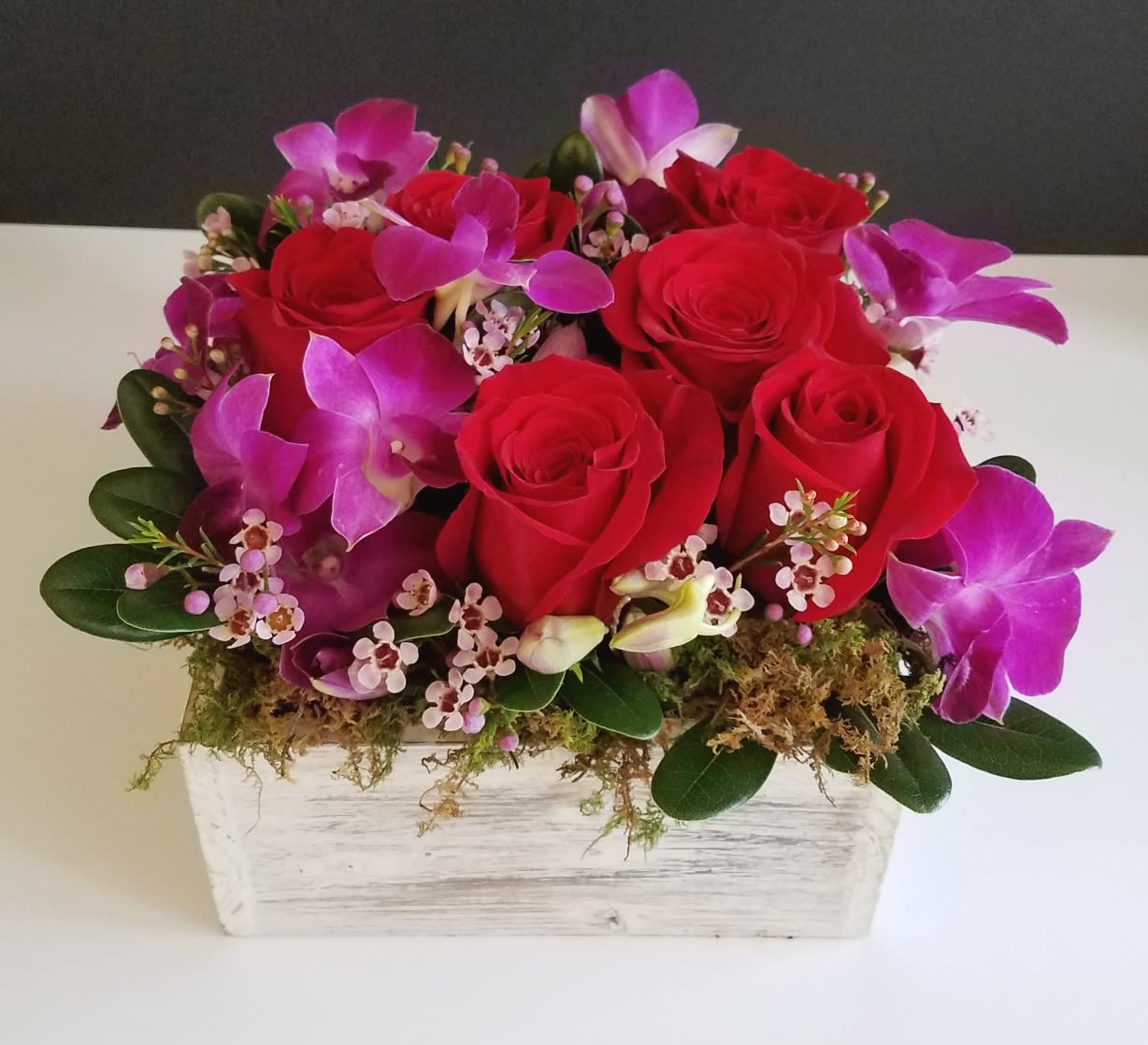 Whisper of Love Whisper of Love - This elegant and modern style wooden box is filled with a romantic assortment of red roses and purple orchids with fillers and greens and finished with moss.