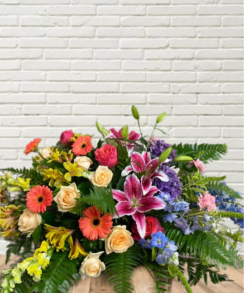 Bright In The Sky Casket Spray Bright In The Sky Casket Spray - A vibrant display to represent your loved one! With roses, stargazers, gerbera daisies, alstroemeria, hydrangea, delphinium, and carnations.