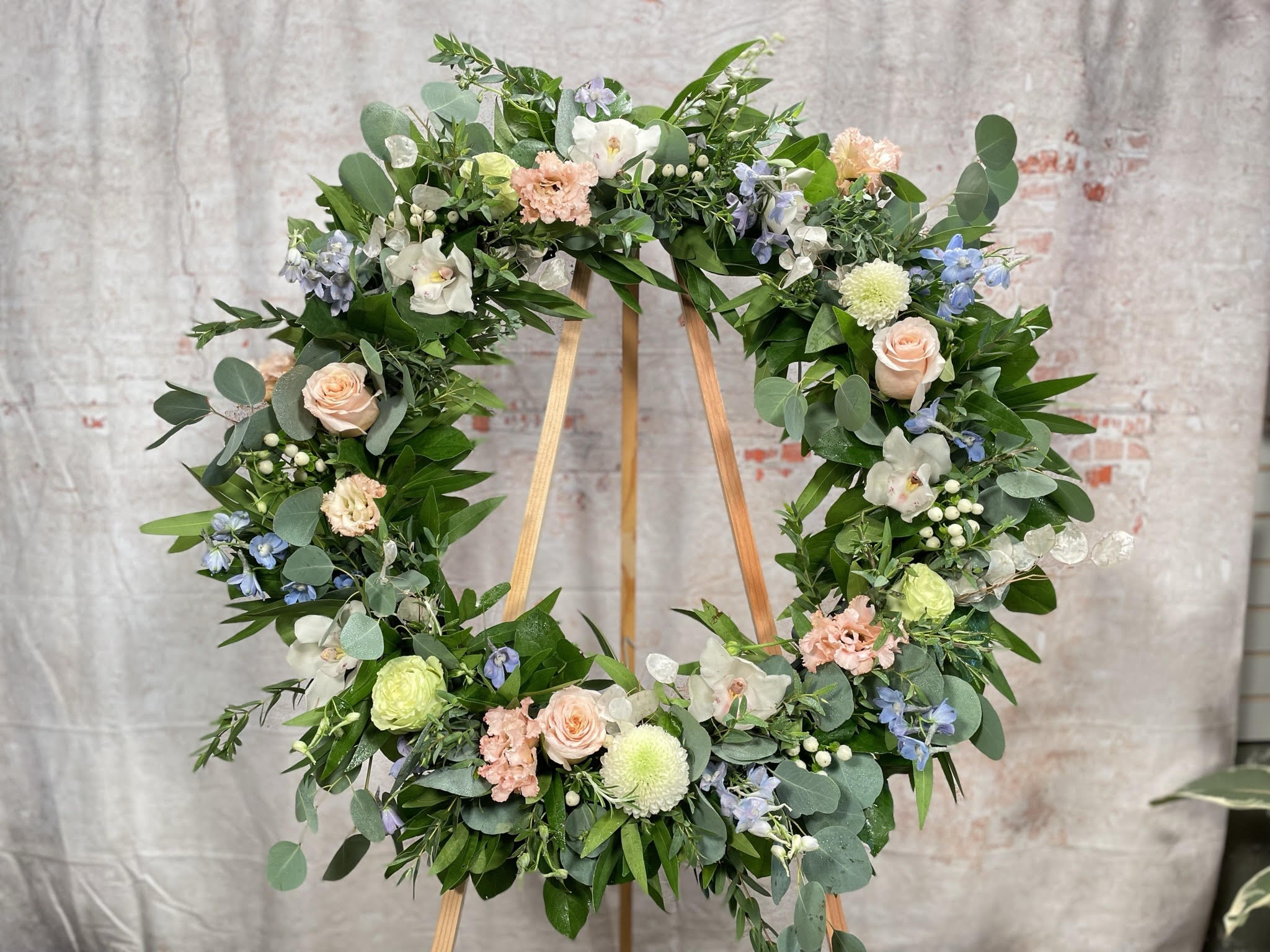 Cherished Wreath - Blue is for sorrow, and white is for hope. A beautiful wreath to honor the memory of a loved one featuring blue delphinium, white roses, white orchids, mixed greenery, a touch of peach. Airy and gardeny. 