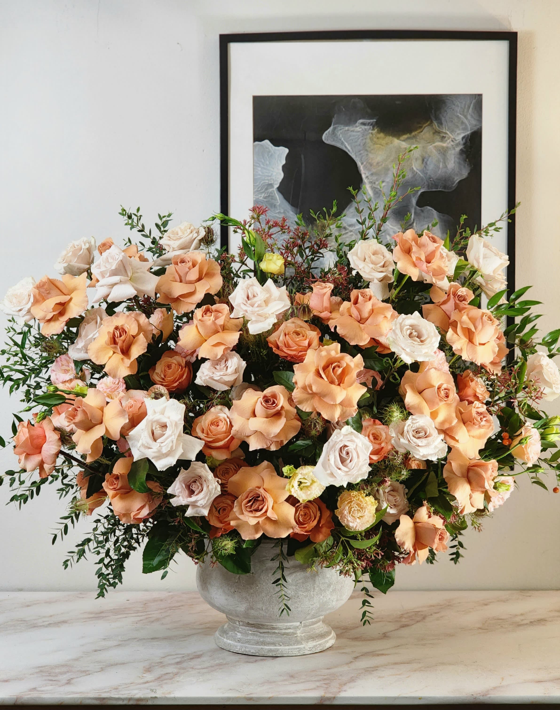 Grandiosa Versaille Garden  - A grandiose vase holds an enchanting blend of beige and peach roses, their petals delicately unfurling in harmonious elegance. The air is kissed with the subtle, soothing fragrance of eucalyptus, creating a sensory symphony that transforms the space into a beautiful world of natural grace and allure.