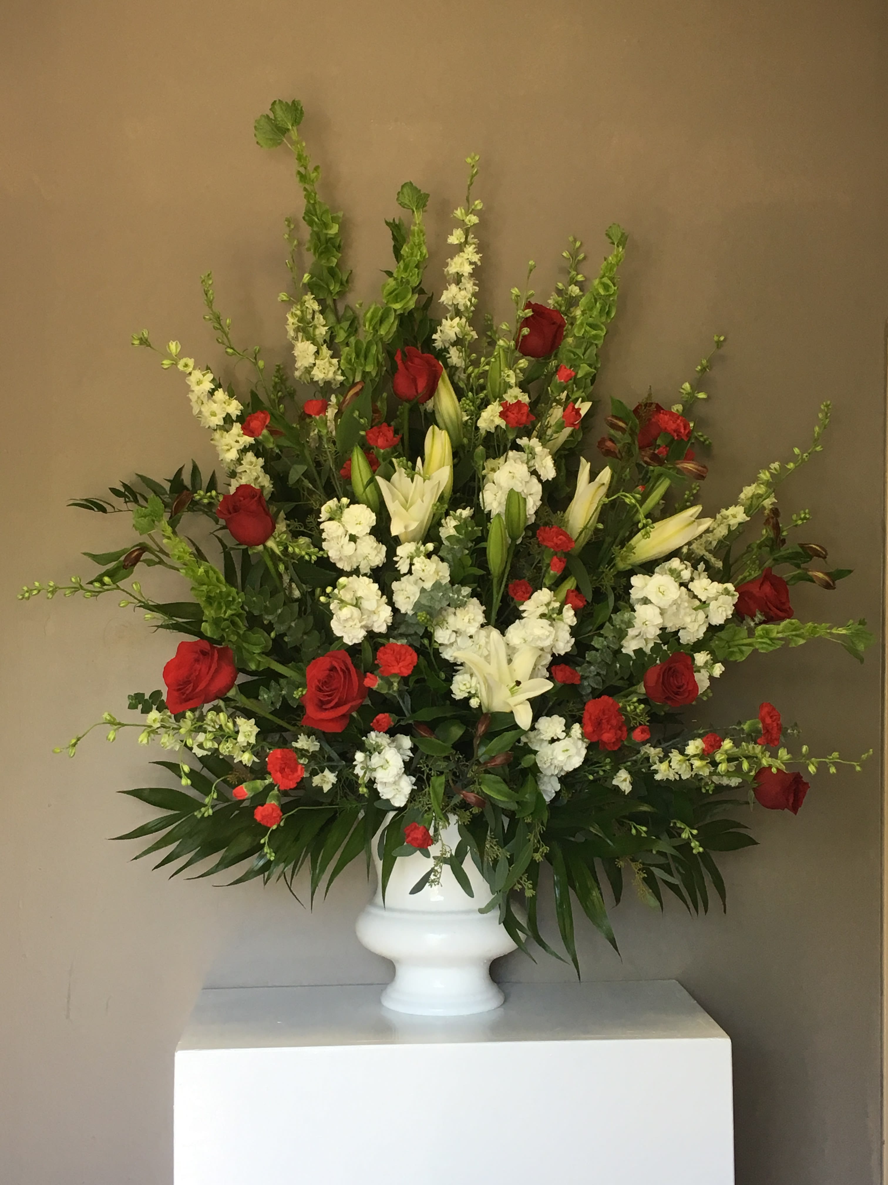 Rosey Red - Red Roses, Red Carnations, White Lilies, White Delphinium, White Stock, with a Ring from the Bells of Ireland Arranged in an Arrangement for Any Occasion 