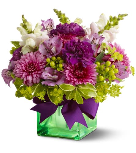 Teleflora's Cheerful Wishes - Lift a good friend's spirits with a lovely lavender and green bouquet and send cheerful wishes their way! A range of blossoms in gentle shades of purple and chartreuse - presented in a green glass cube vase - is the perfect pick-me-up. A purple satin ribbon adds a pretty touch. A mix of fresh flowers such as chrysanthemums carnations snapdragons and alstroemeria in shades of lavender purple and pink ? accented with greenery ? is arranged in a Teleflora green glass cube vase tied with a purple ribbon. Approximately 9&quot; (W) x 10&quot; (H) Orientation: All-Around As Shown : TFWEB318