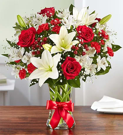 Fields of Europe® for Christmas - Inspired by the beauty of the European countryside, our best seller brings together radiant roses and lush lilies in a glass vase wrapped in red ribbon. Whatever your reason for reaching out, it’s a gift that delivers on delight. All-around arrangement with red roses and mini carnations; white Asiatic lilies and Peruvian lilies (alstroemeria); accented with baby’s breath, hypericum and assorted greenery To ensure lasting beauty, Asiatic and Peruvian lilies may arrive in bud form and will fully bloom over the next few days