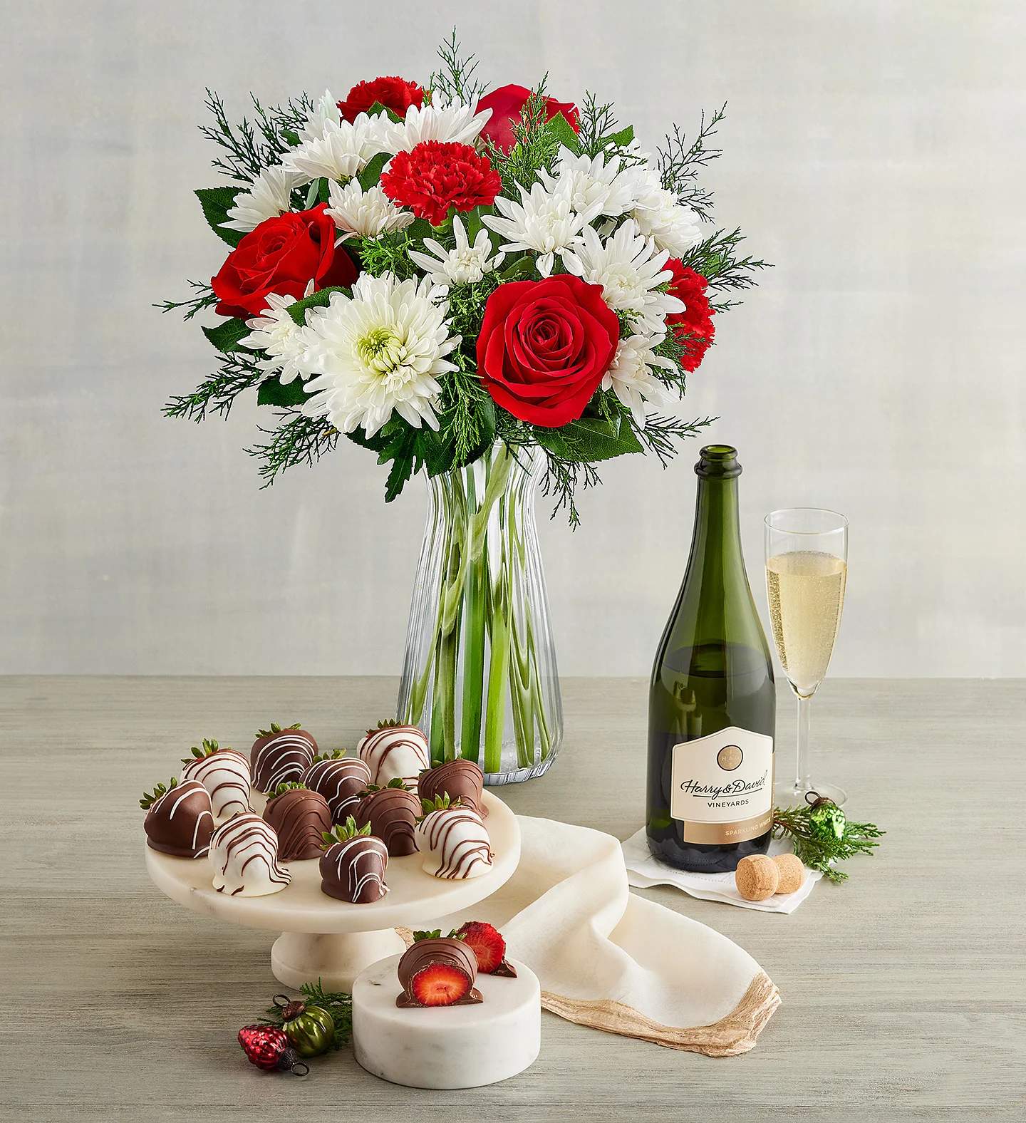 Holiday Celebrations Bouquet and Wine - This beautiful bouquet is brought together with a wine and a dozen chocolate covered strawberries.  This arrangement comes with 3 red roses, 3 red carnations, 3 white mums, 3 white cushion, and christmas greens.