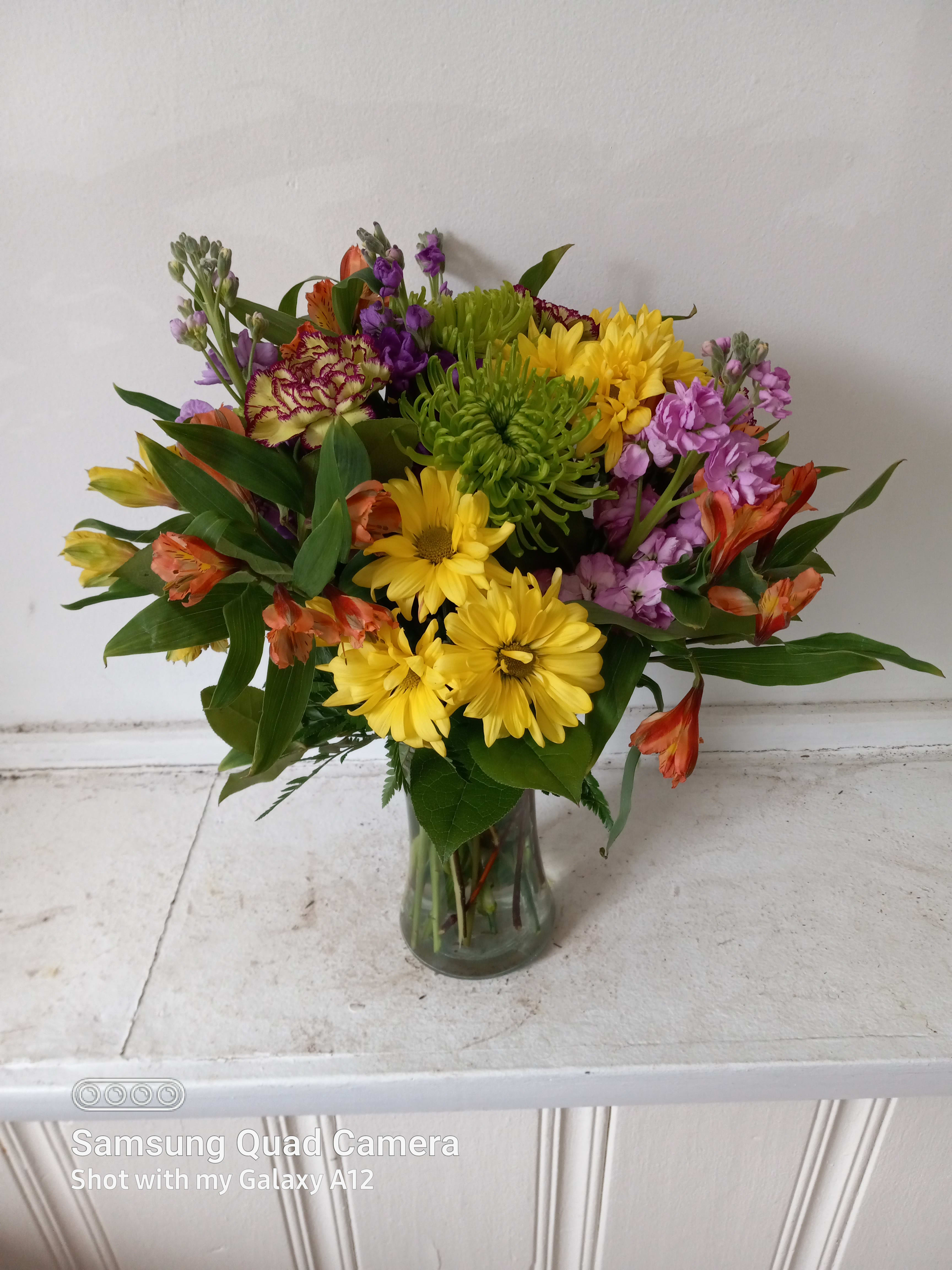 Marmalade sky  - Beautiful blush mix of orange roses, alstroemeria, yellow cushion pompons, purple stuck, green Fuji mums and purple Fresia in a vase 