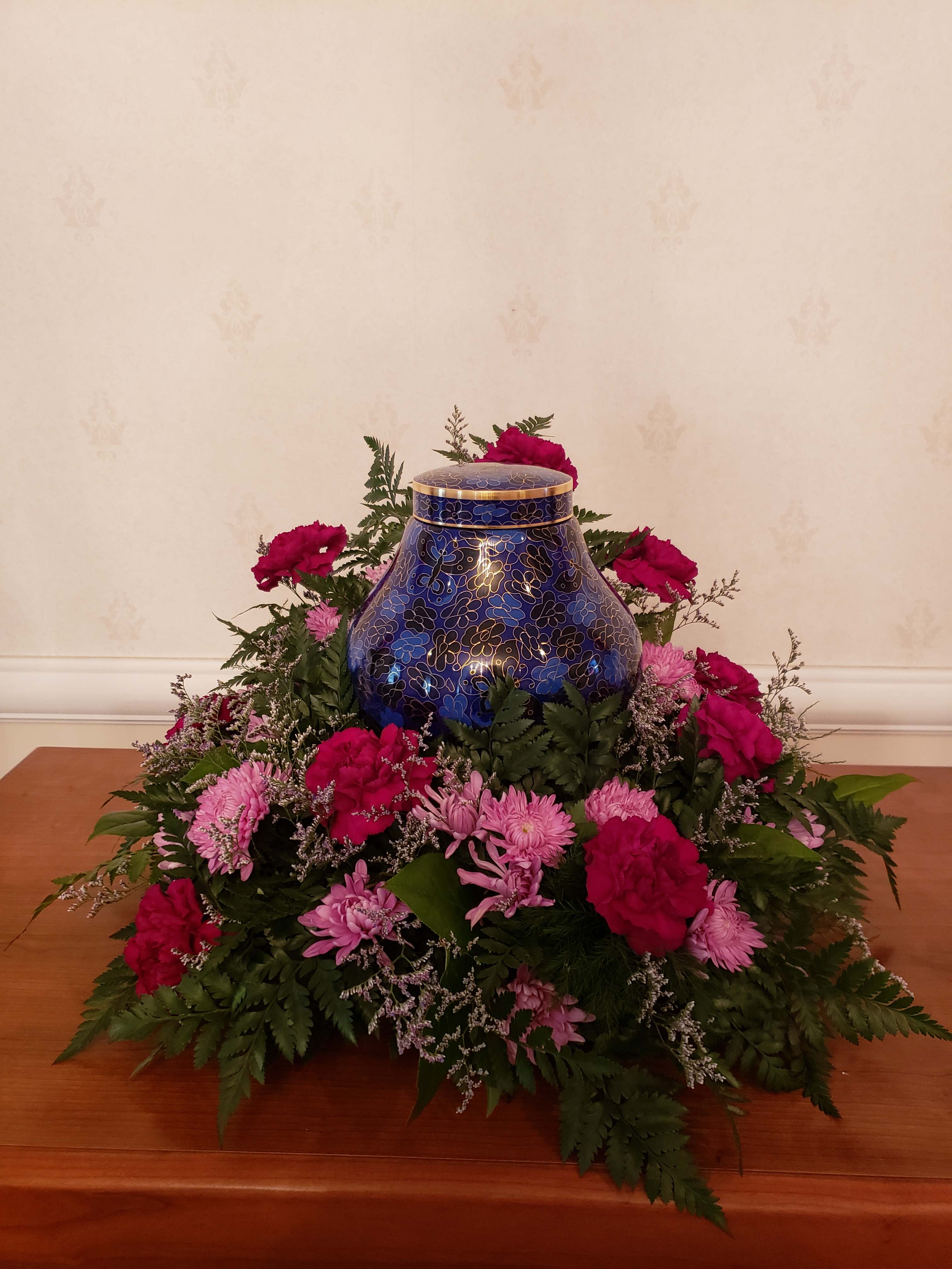 TPP-SR01 - Stadium Crown Urn Ring with magenta carnations, lavender cushions, and pops of limonium throughout. Complete with various greens. Urn sets in center and can be placed on a riser to enhance look. 