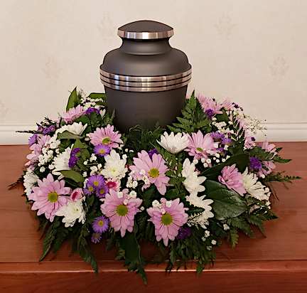 TPP-RR01 TPP-RR01 - A simple yet elegant round urn wreath of lavender daisies, white cushions, purple monte casino and pops of babies breath and statice. Charming and sophisticated. Lavender roses can be added to the deluxe version for added elegance.